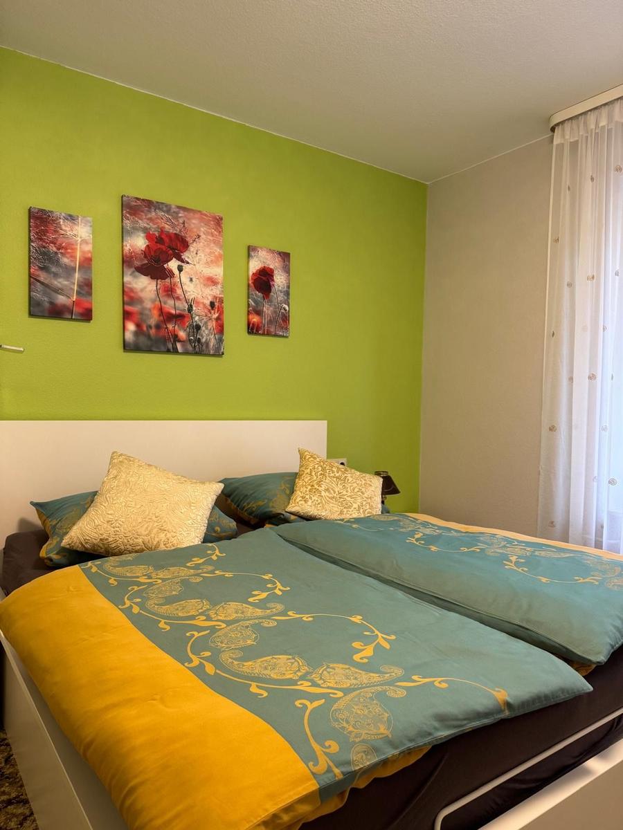 Schlafzimmer mit Bett, grüner Wand und drei Wandbildern mit roten Mohnblumen.