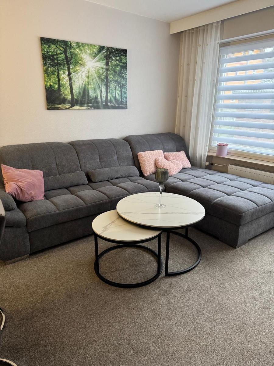 Ein Wohnzimmer mit grauem Sofa, zwei runden Tischen und einem Wandbild.