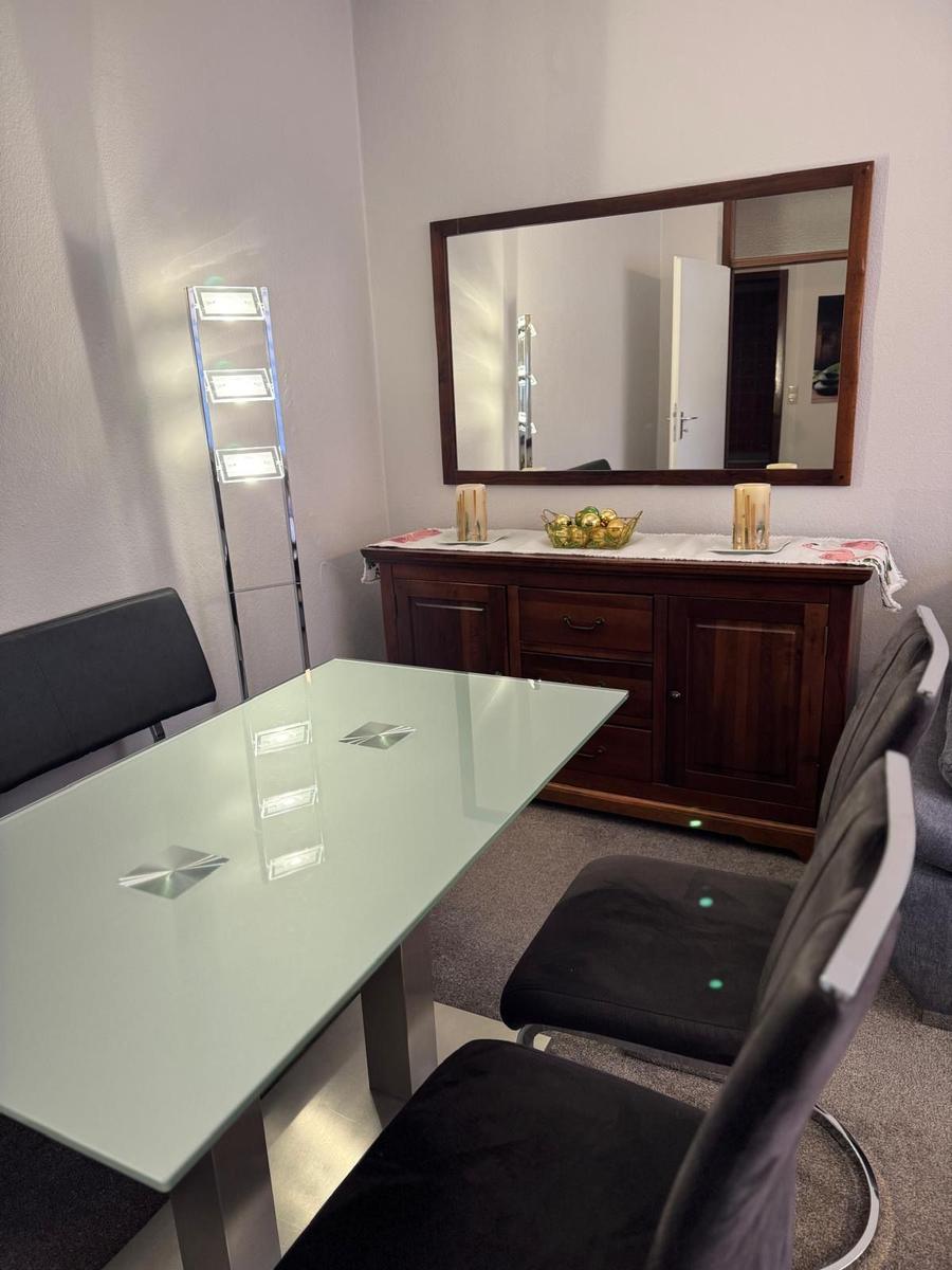 Essbereich mit Glas-Tisch, schwarzen Stühlen und Holzschrank mit Spiegel.
