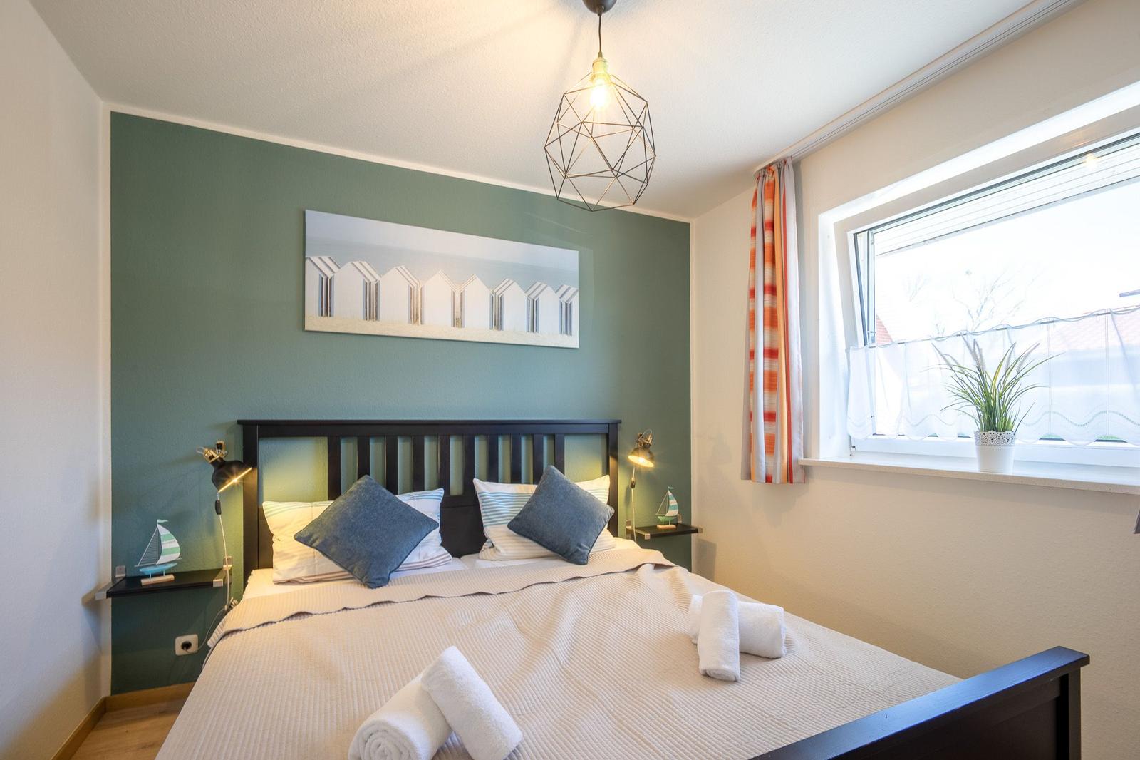 Schlafzimmer mit Bett, Nachttischen und Fenster mit Pflanze.