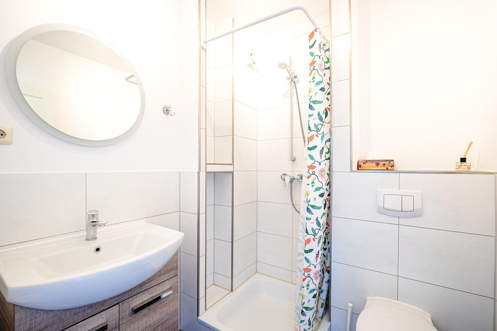 Badezimmer mit Dusche, Waschbecken und Toilette. Duschvorhang mit buntem Muster.