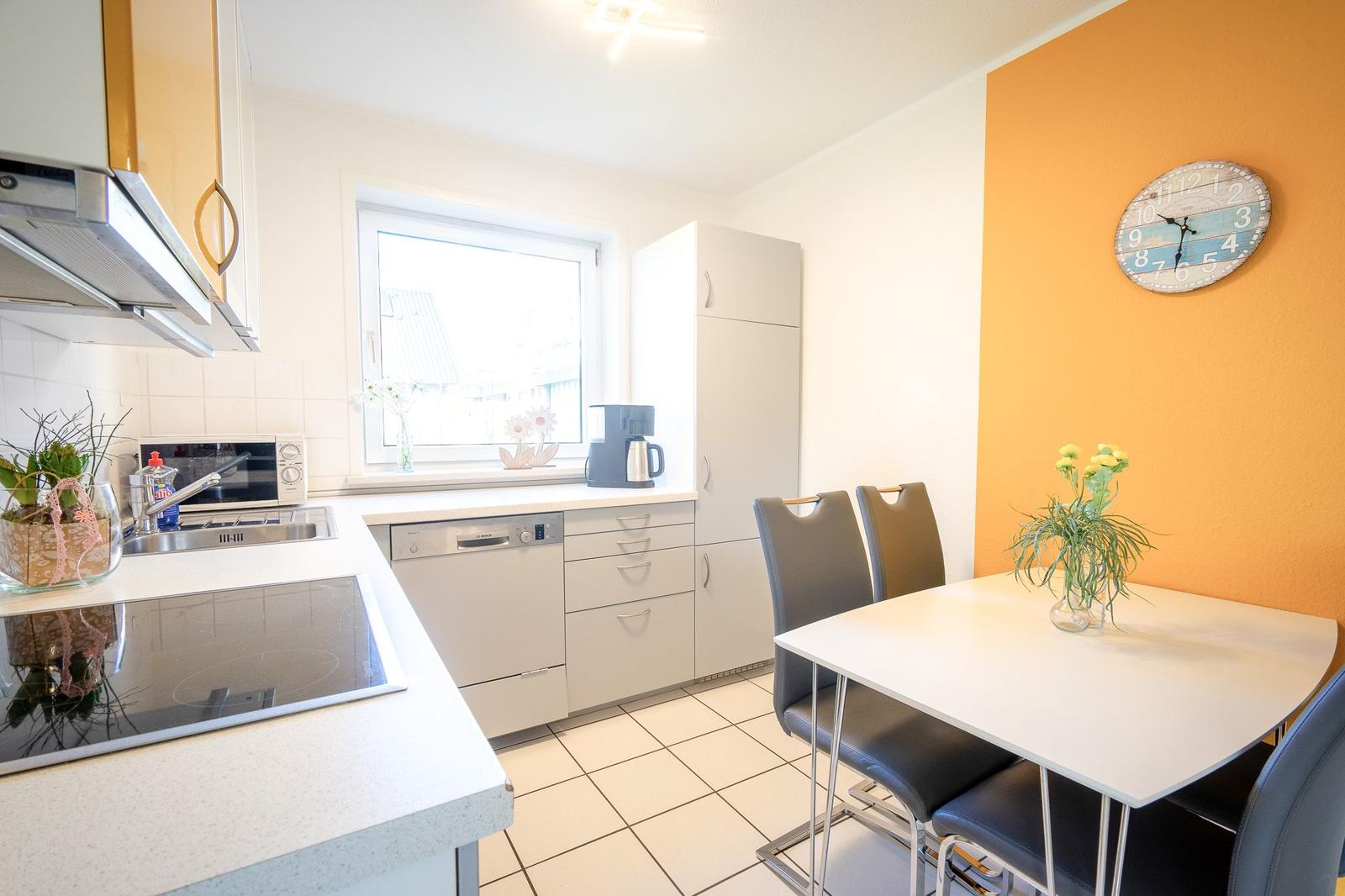 Küche mit Essbereich, weiße Arbeitsflächen, Küchenschränke und eine orange Wand mit Uhr.