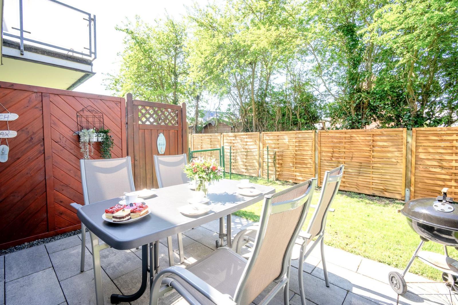 Terrasse mit Tisch, Stühlen, Grill und Blumenarrangement.