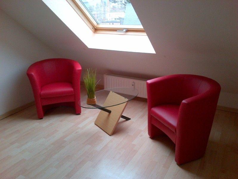 Zwei rote Sessel und ein Glas-Tisch unter einem Dachfenster mit Holzboden.