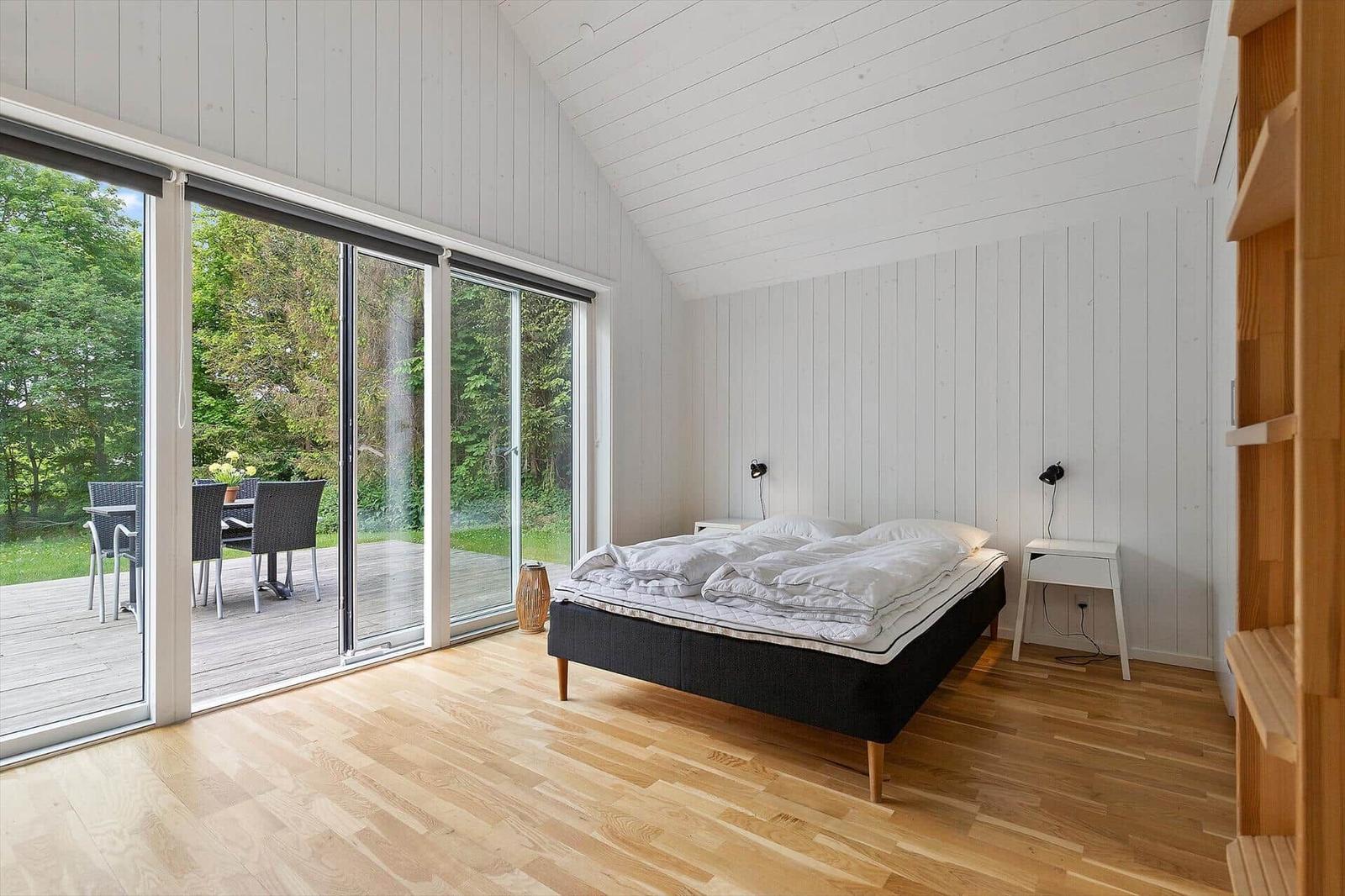 Schlafzimmer mit Balkon, weißer Wandverkleidung und Holzboden.