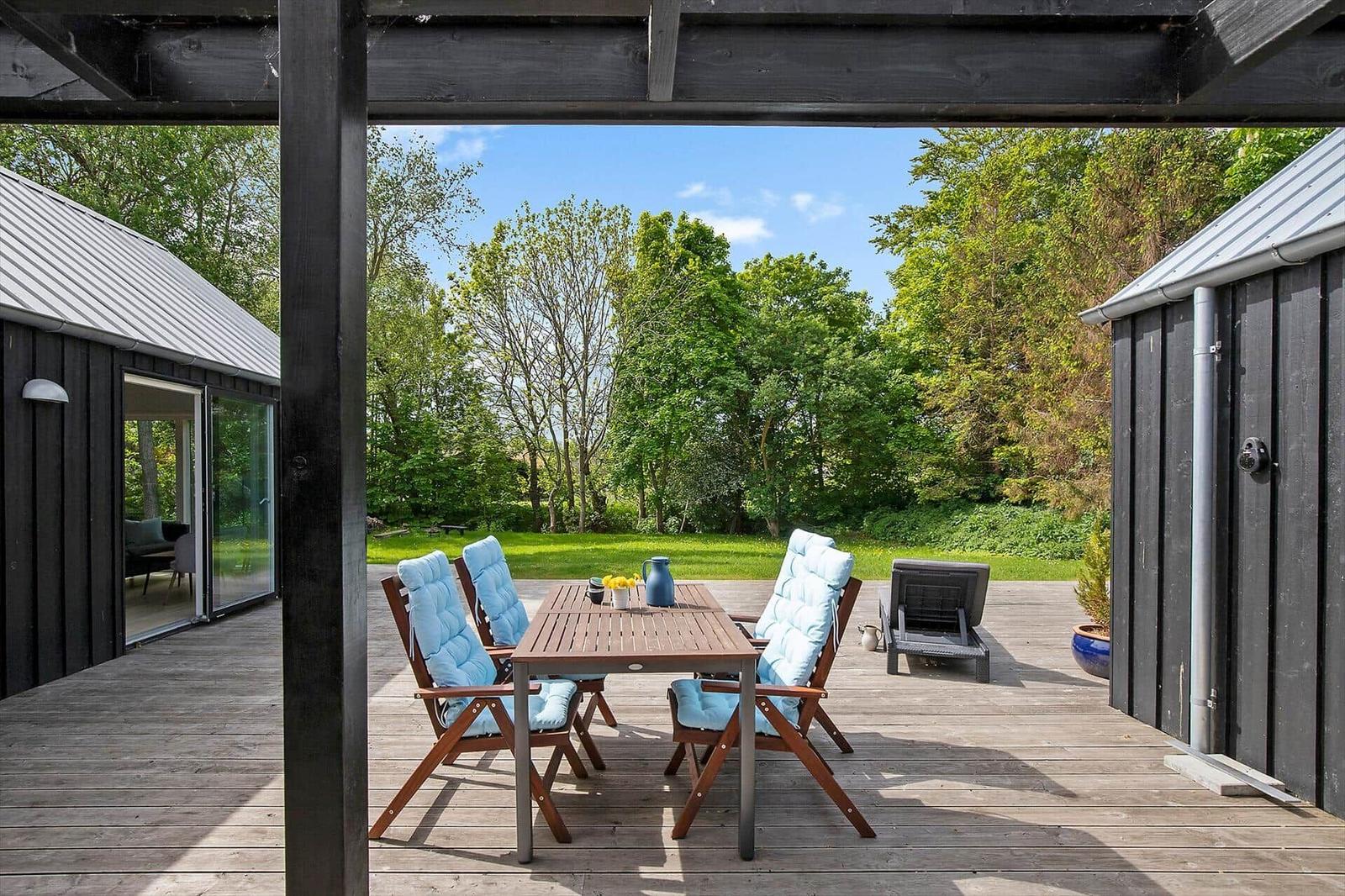 Terrasse mit Tisch, vier Stühlen und blauen Kissen. Hintergrund: grüner Garten und Bäume.