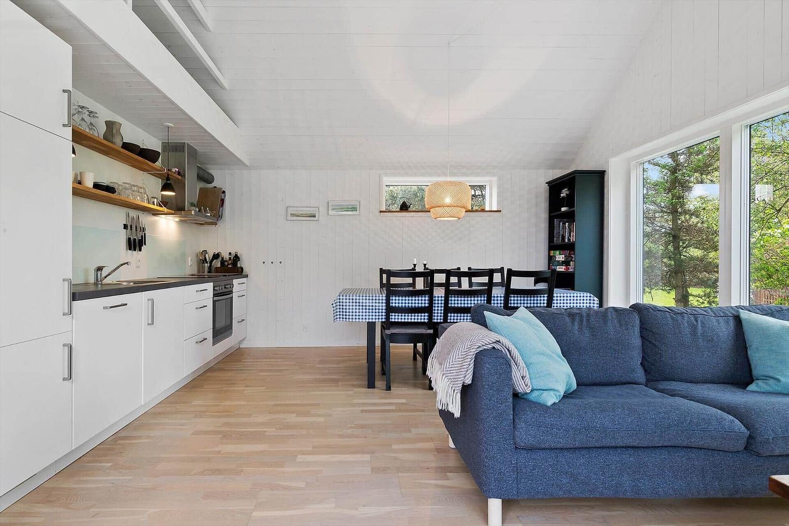Küche, Essbereich und Wohnbereich mit blauem Sofa und Holzboden.