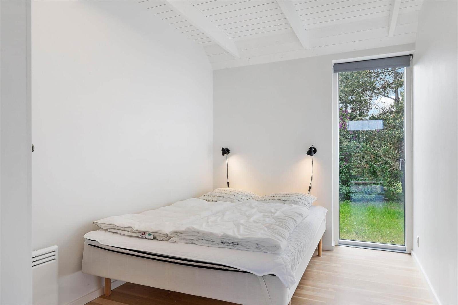 Schlafzimmer mit Bett, zwei Wandlampen und Glasschiebetür zum Garten.