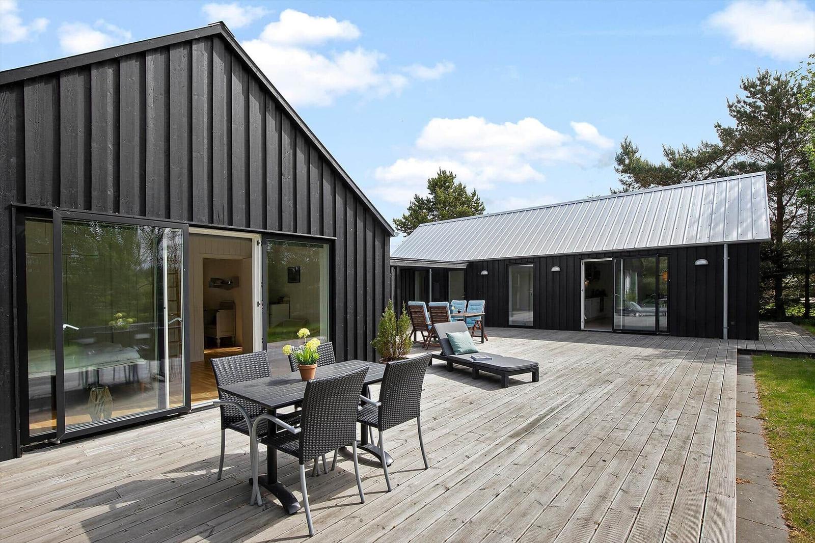 Moderne Holzhütte mit großem Holzterrasse, Sitzgelegenheiten und Garten.