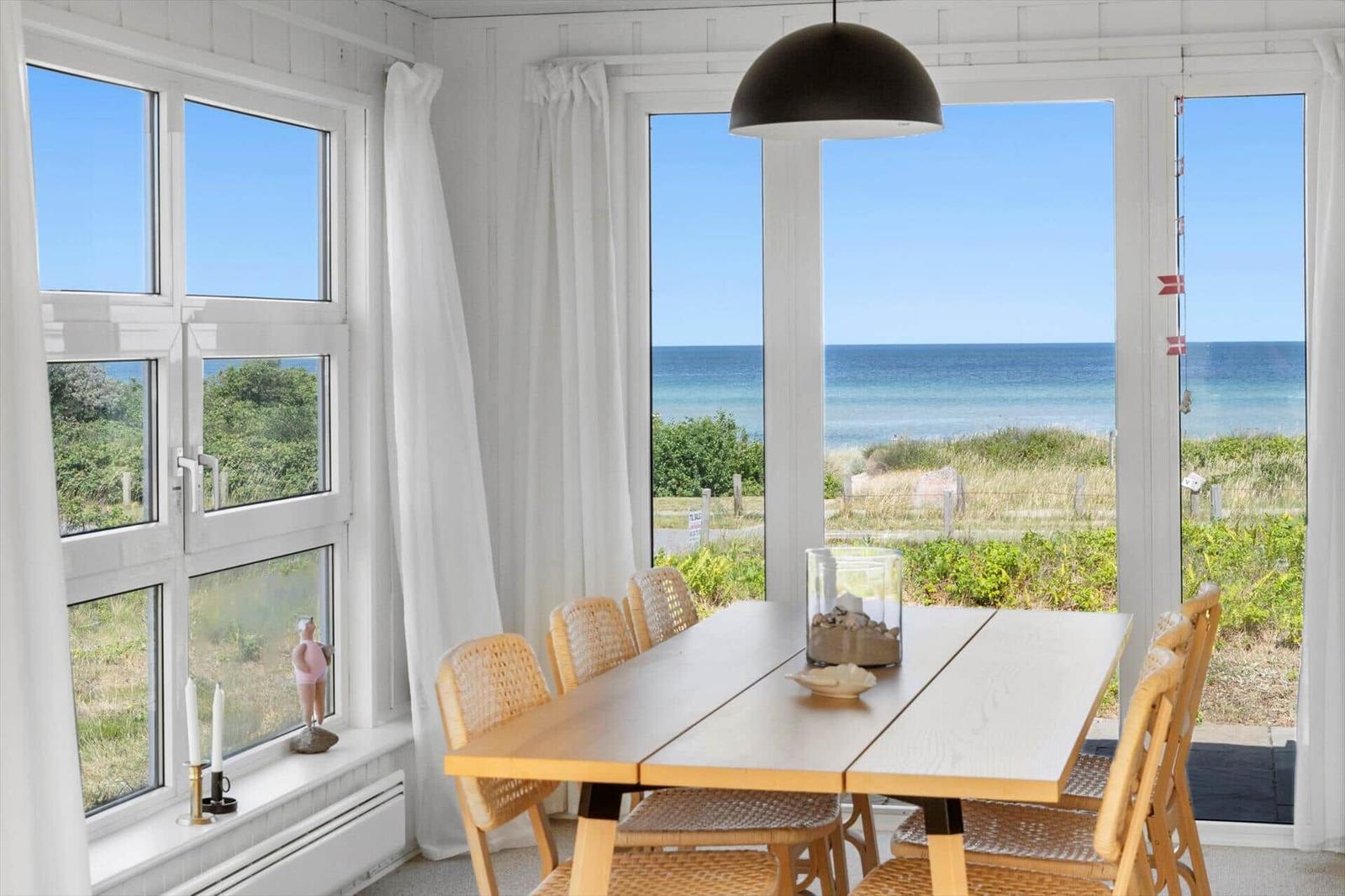 Esszimmer mit Tisch, Stühlen und Meerblick durch große Fenster.