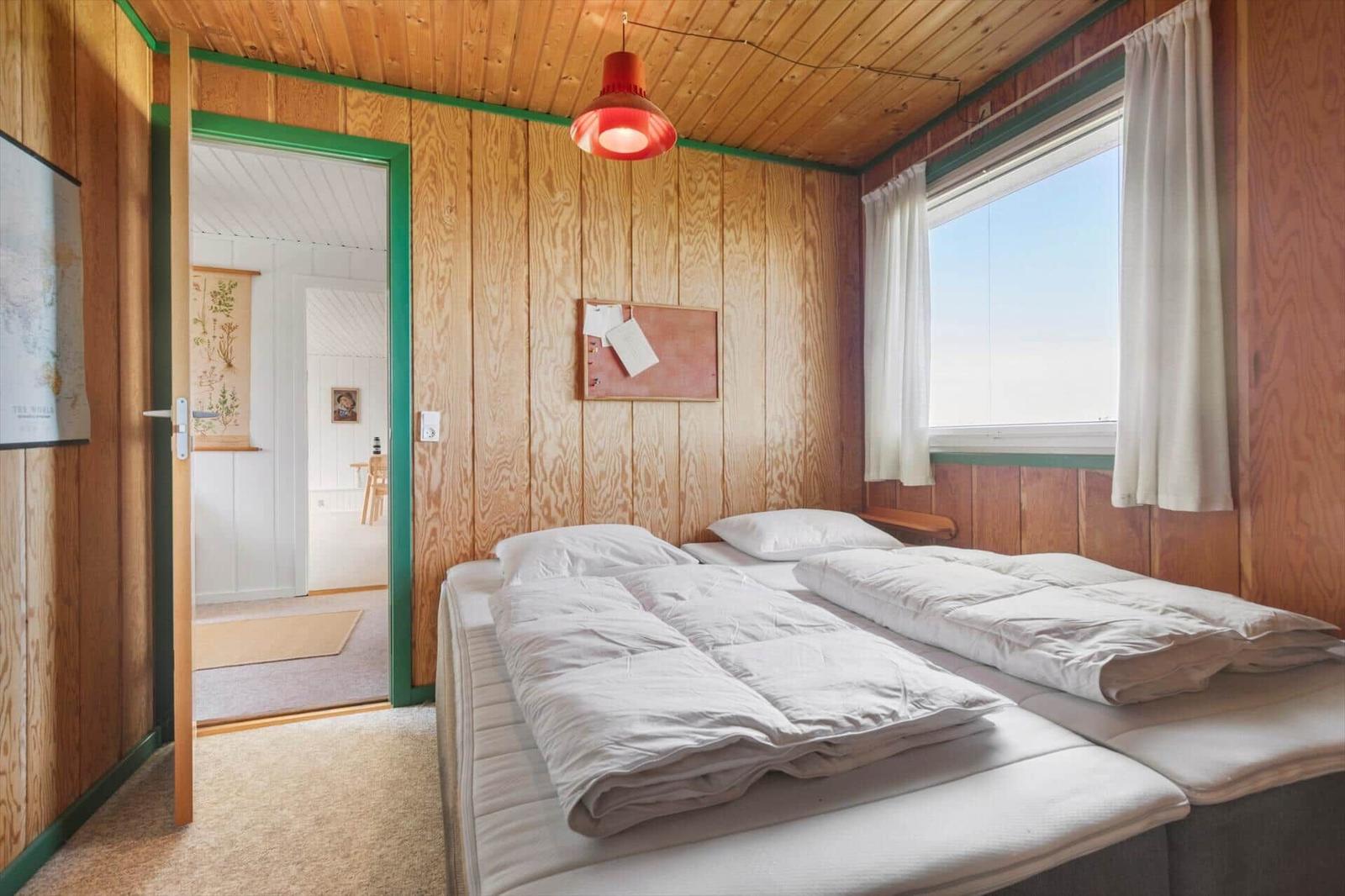 Zwei Betten in einem Raum mit Holzwänden und Fenster. Tür führt in einen anderen Raum.