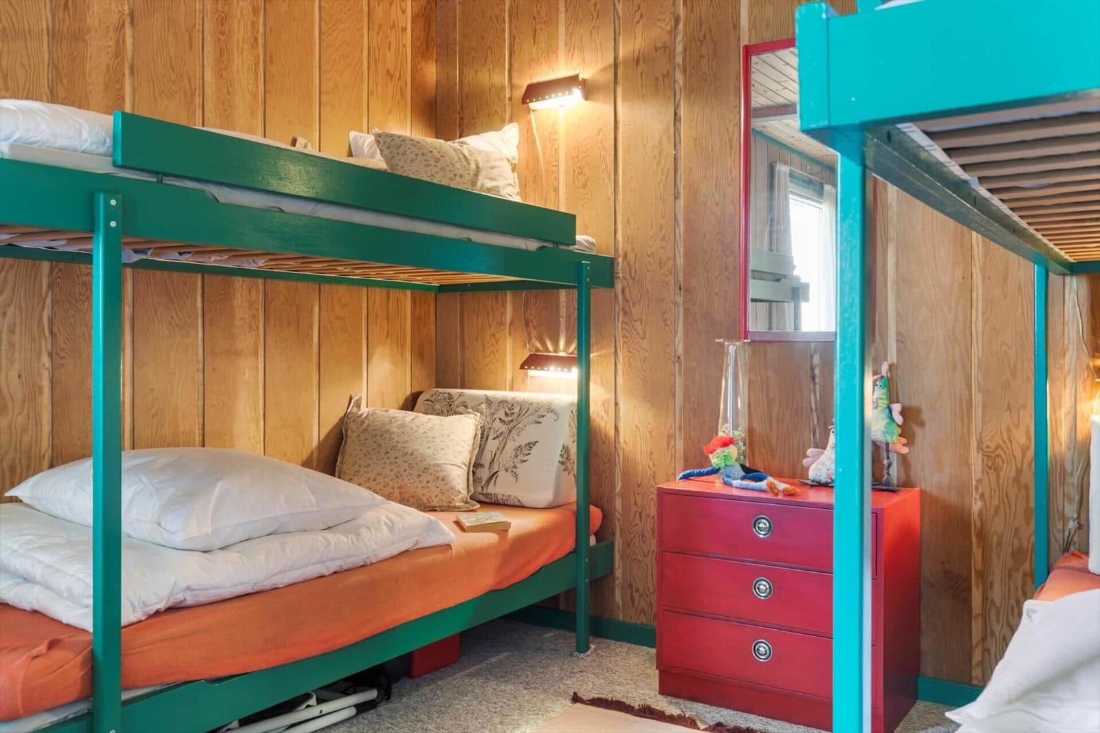 Zimmer mit zwei Etagenbetten, rotem Schrank und Holzwandverkleidung.