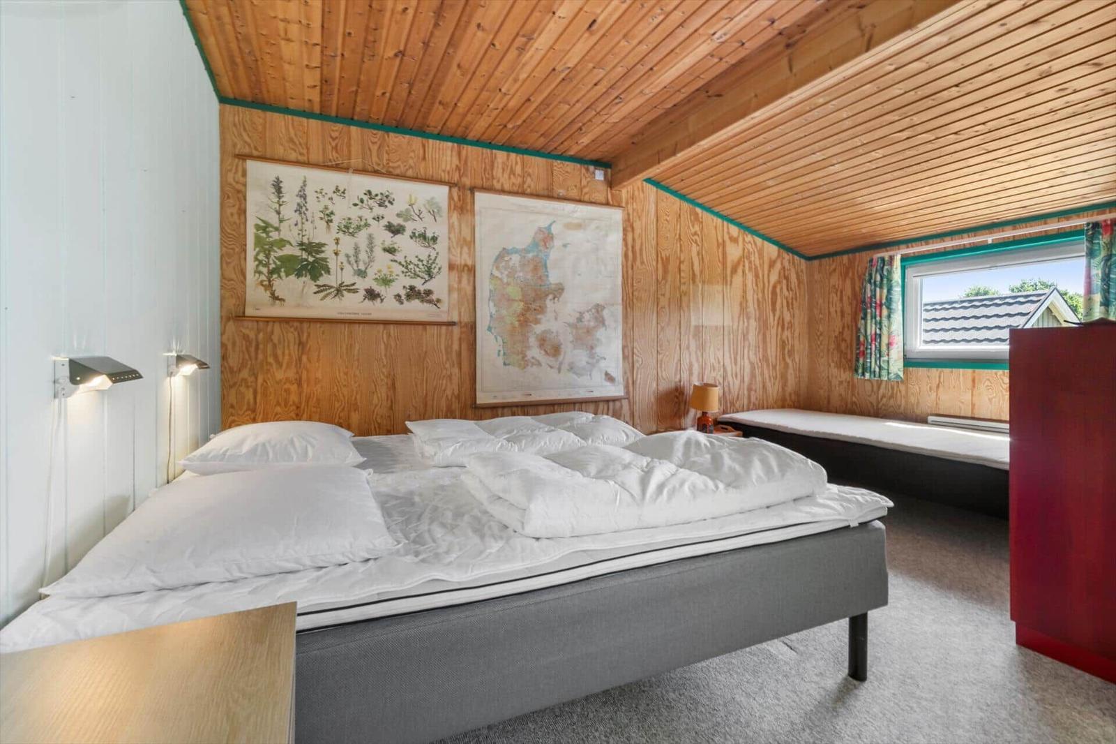 Schlafzimmer mit Doppelbett, Holzwand und Fenster. Zwei Wandbilder und Nachttische.