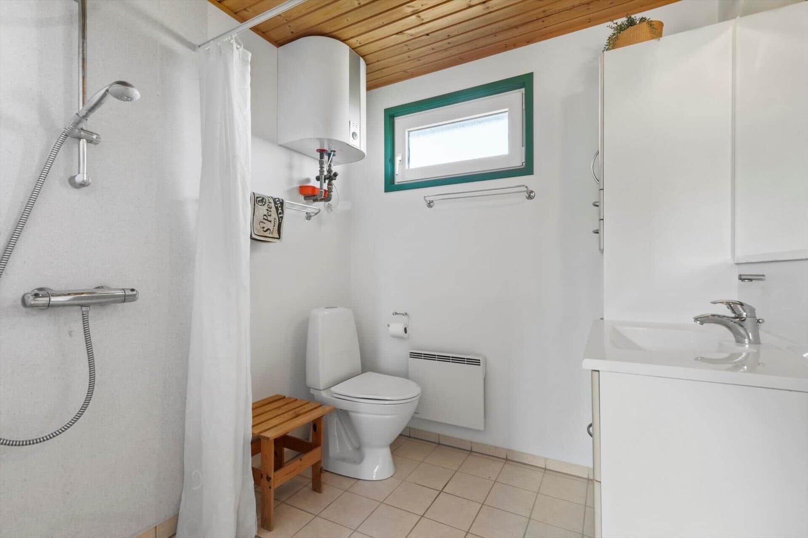 Badezimmer mit Dusche, Toilette und Waschbecken. Holzdecke und grünes Fenster.