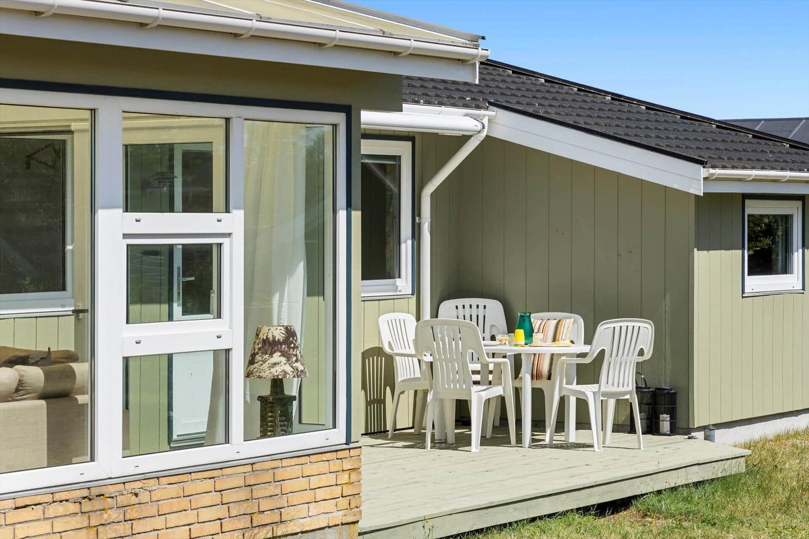 Terrasse mit weißem Tisch und Stühlen vor einem Haus mit Fenster und Terrassentür.