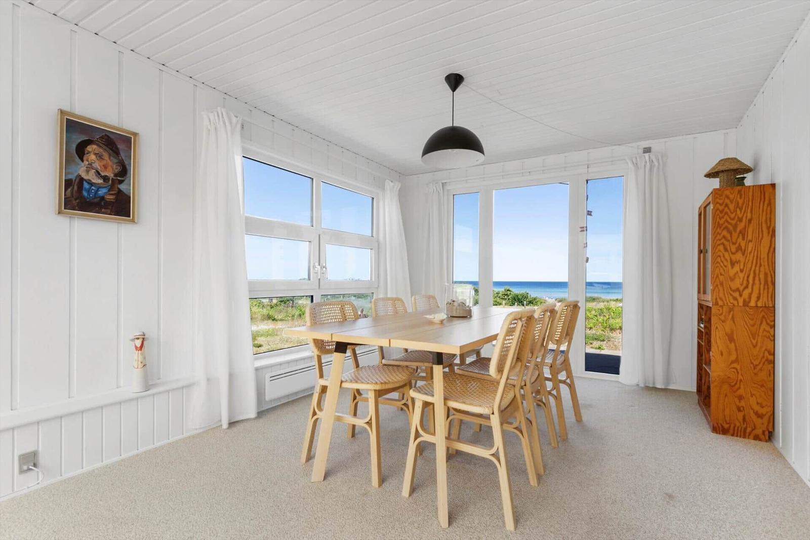 Esszimmer mit Tisch, Stühlen und Meerblick durch große Fenster.