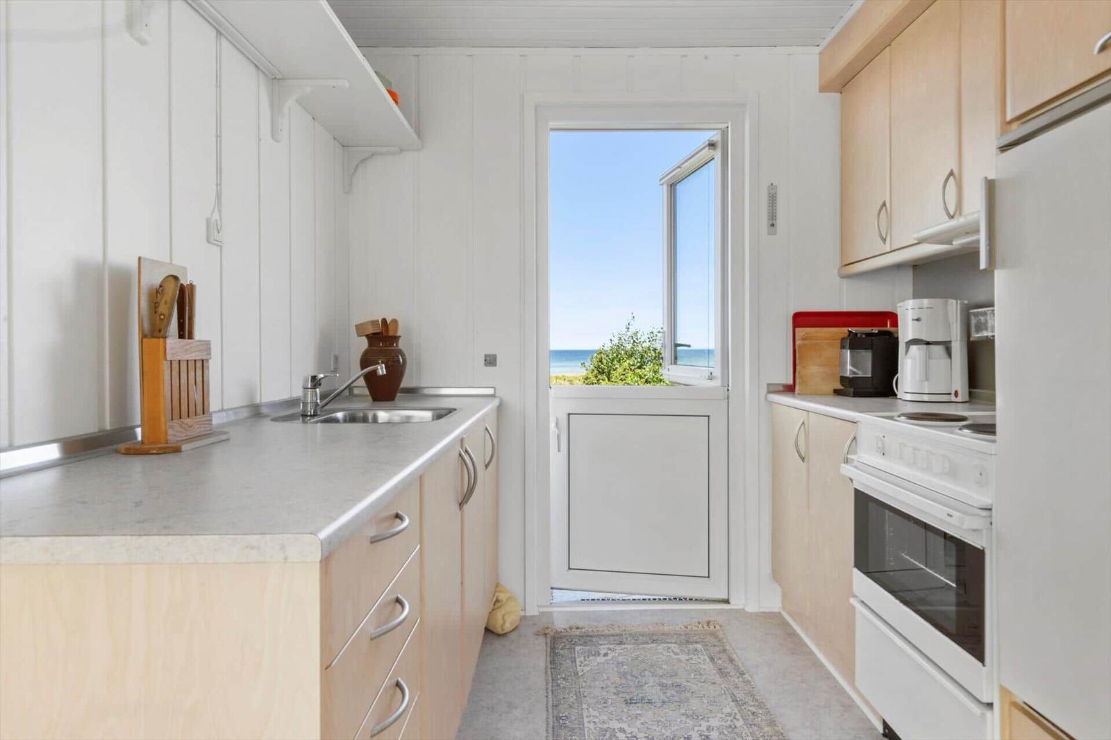 Küche mit Blick aufs Meer, weiße Geräte und Holzschränke.