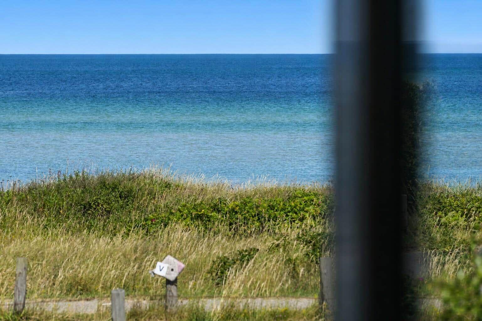 Meeransicht durch Fenster mit Gras und Holzpfosten im Vordergrund.