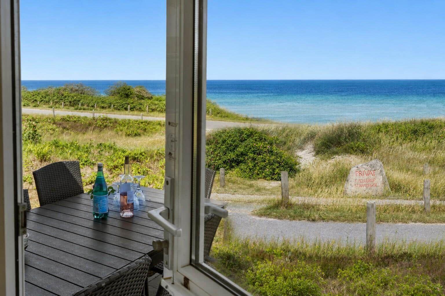 Terrasse mit Tisch und Stühlen bietet Blick auf Meer und Strand.
