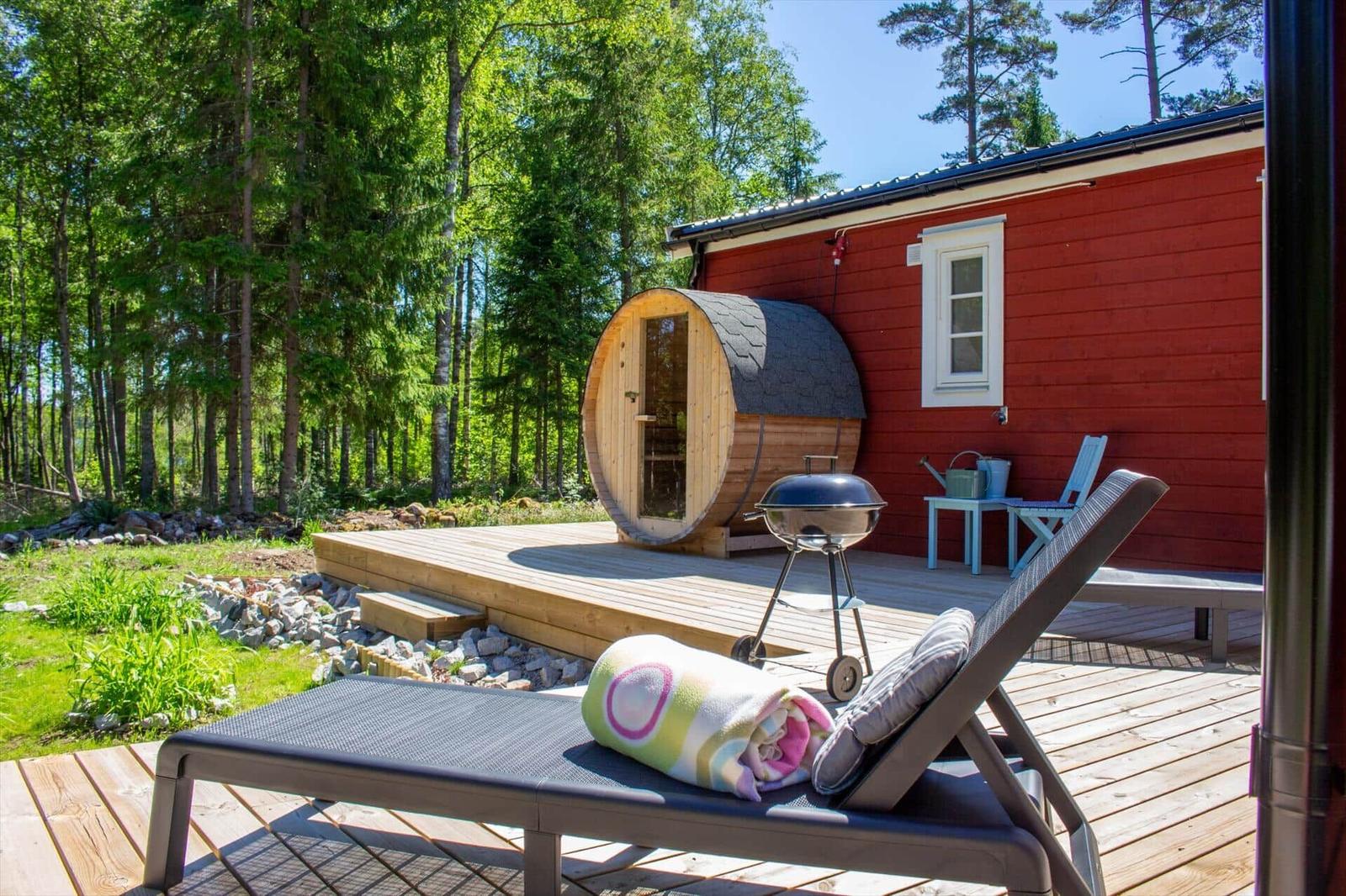 Roter Holzaufbau mit Sauna, Grill und Liege auf Terrasse im Wald.