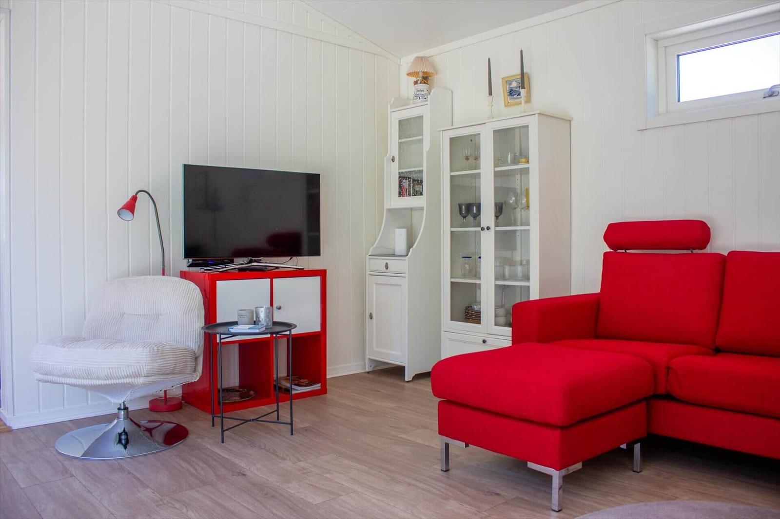 Ein Wohnzimmer mit rotem Sofa, weißer Wand und TV auf rotem Möbel.