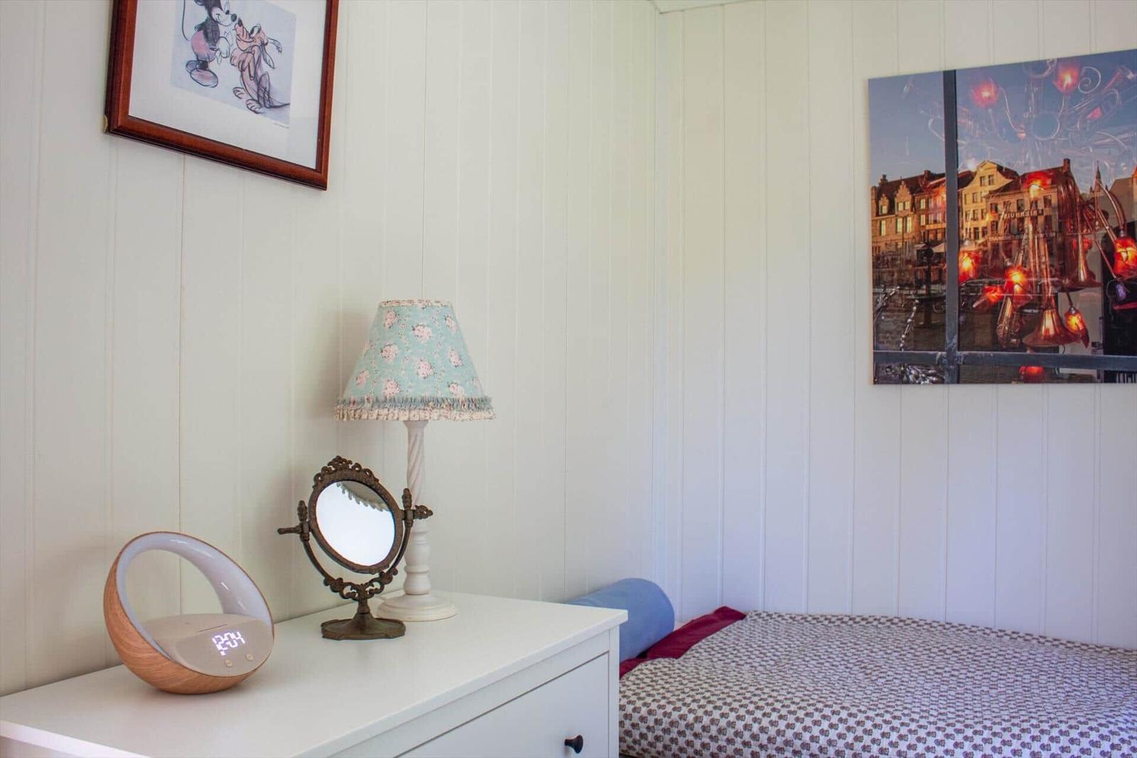 Schlafzimmer mit Bett, Nachttisch, Lampe und Wandbildern.