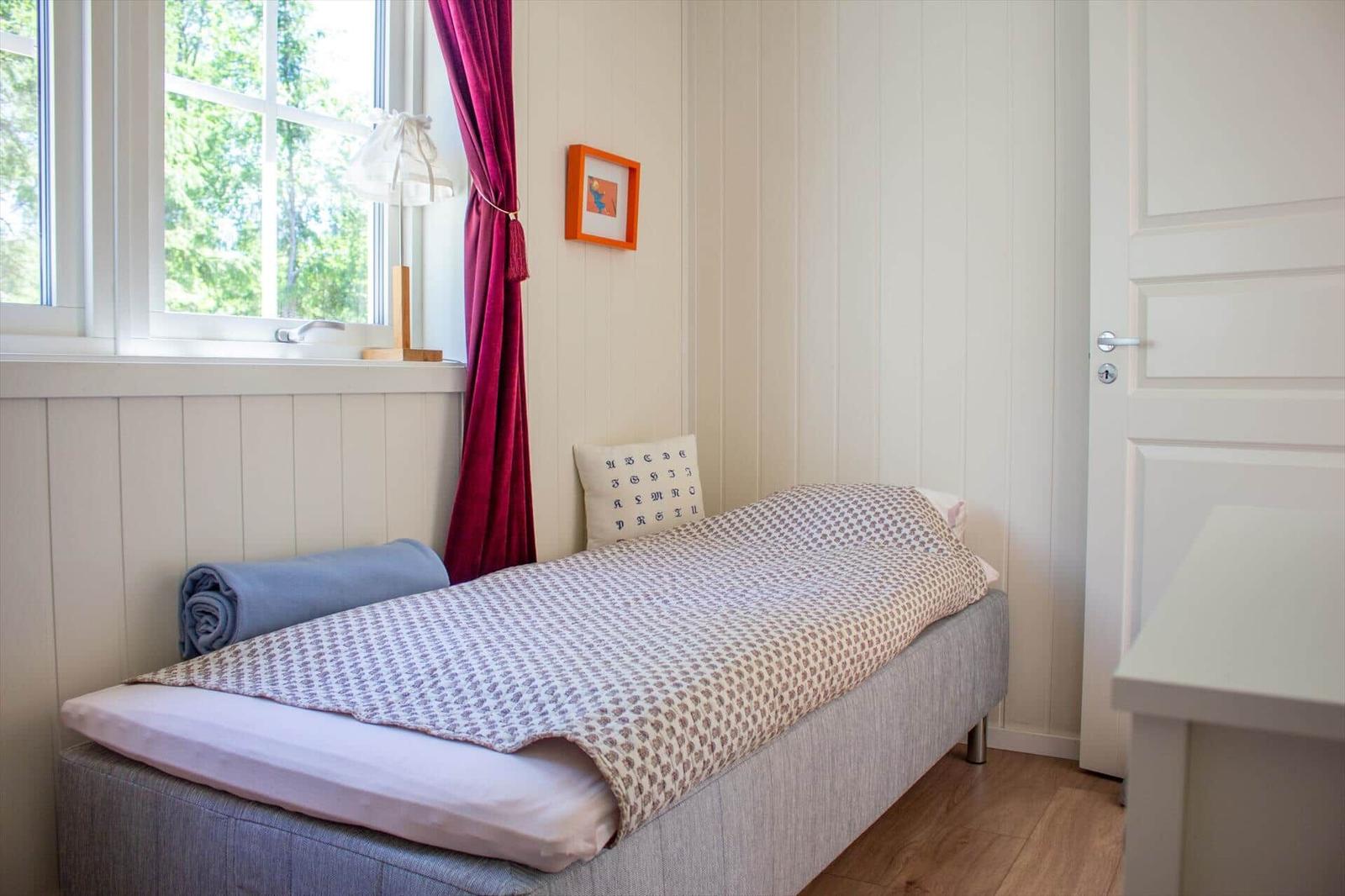 Ein Schlafzimmer mit Bett, Fenster und Tür. An der Wand hängt ein Bild.
