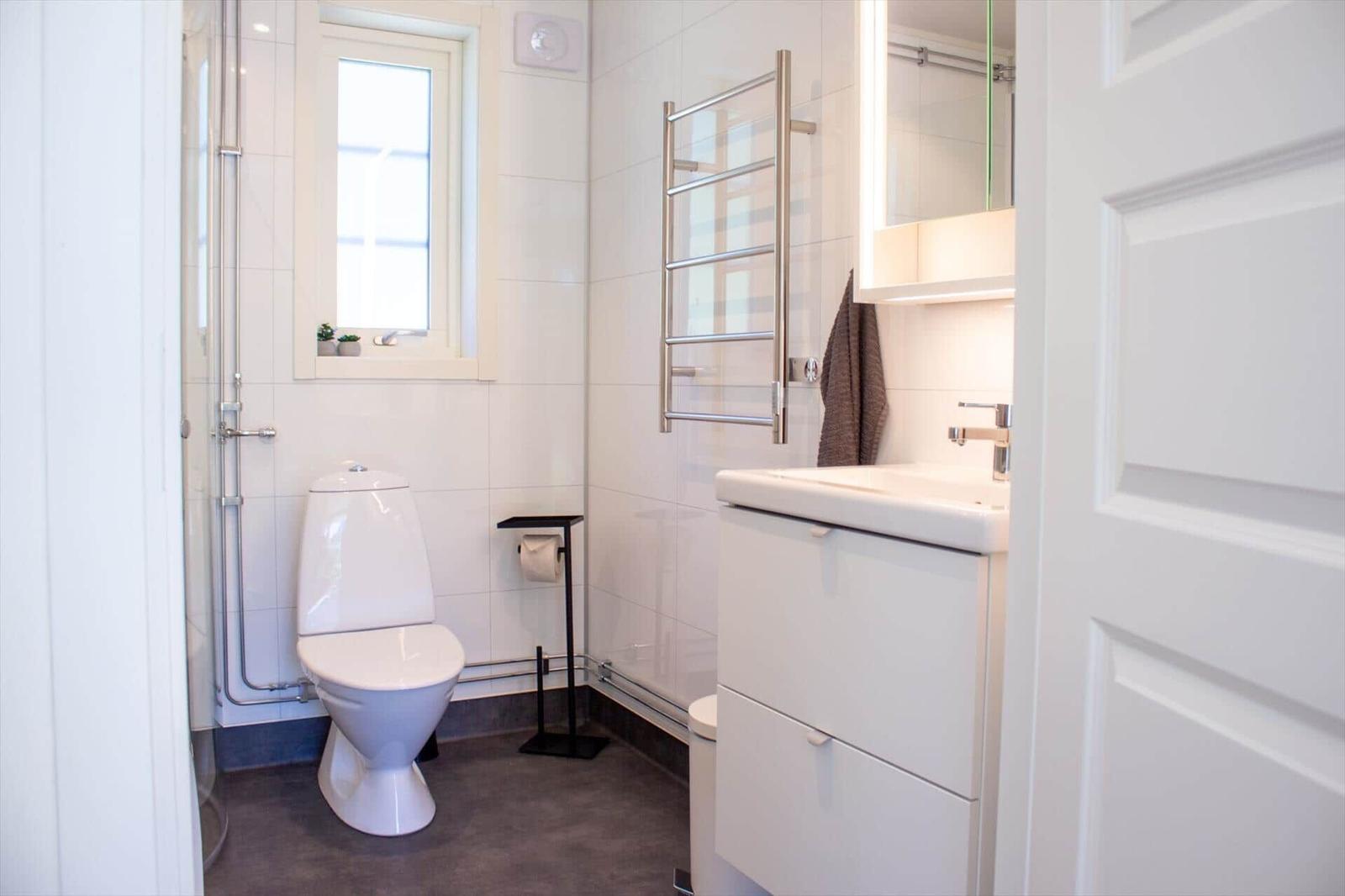 Badezimmer mit Toilette, Waschbecken und Dusche. Fenster, Handtuchhalter und Spiegel sichtbar.