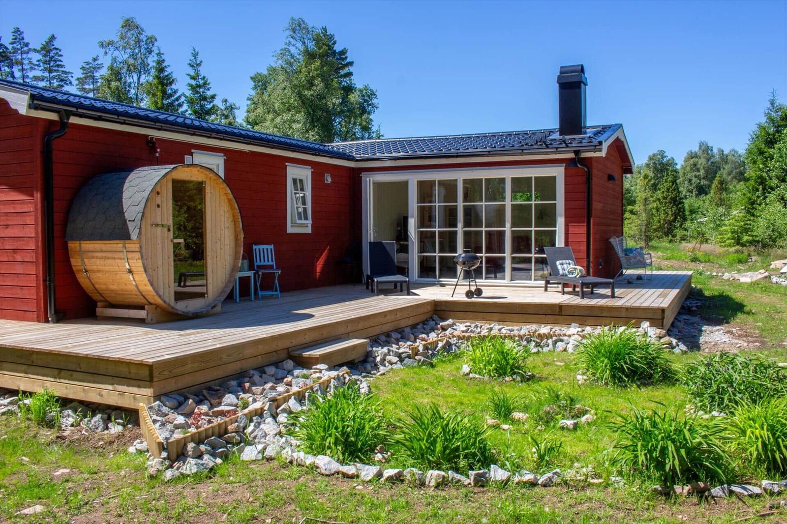Rotes Holzhaus mit Terrasse, Sauna und Grillplatz im Grünen.