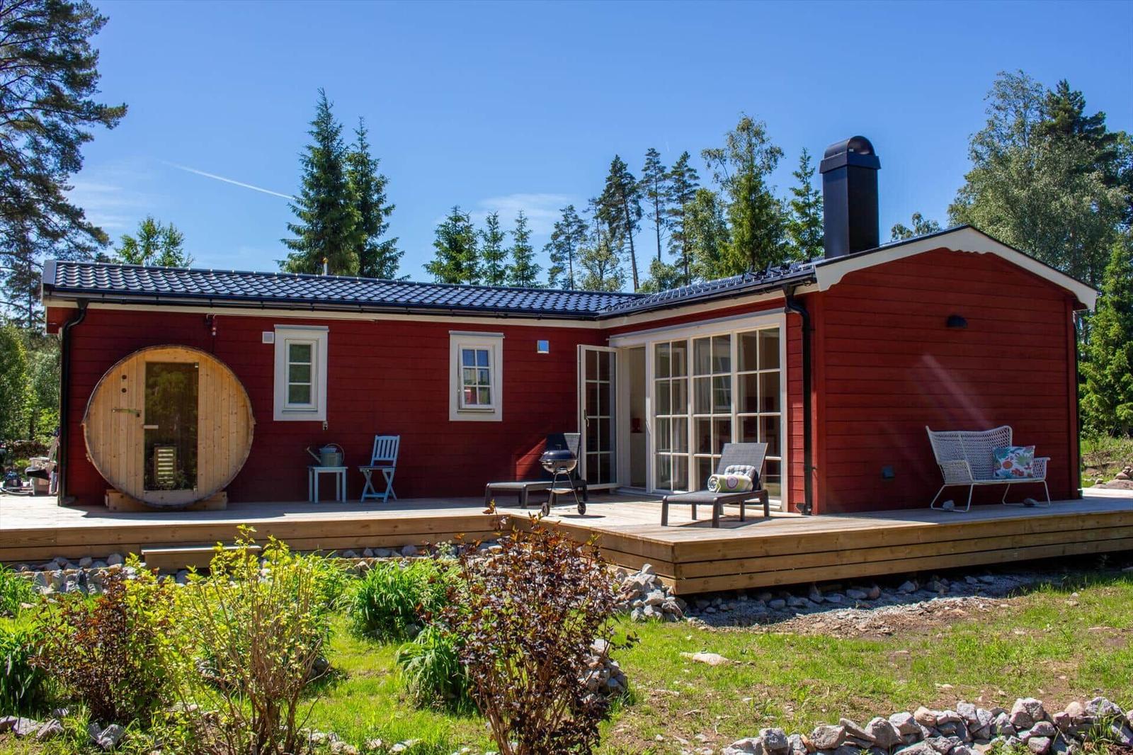 Rotes Holzhaus mit Terrasse, Sauna und Garten. Grill und Sitzmöbel auf der Veranda.