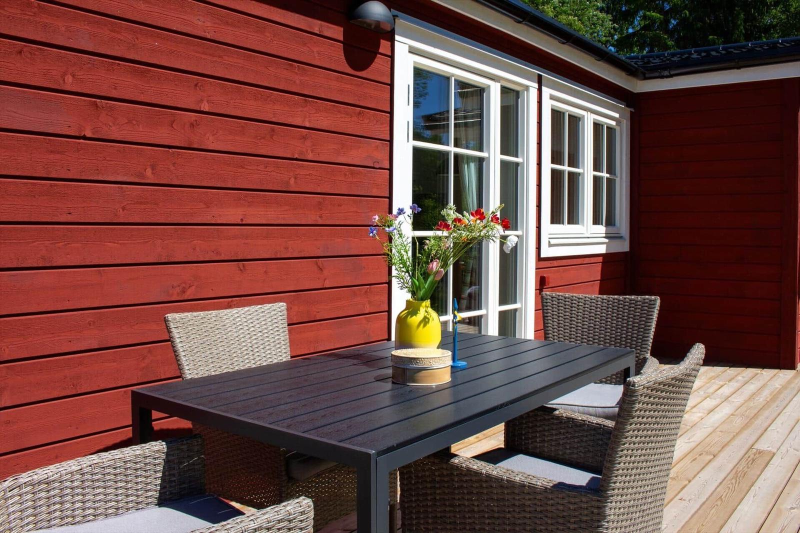Roter Holzaufbau mit Terrasse, Tisch und Stühlen sowie Blumen in einem Topf.