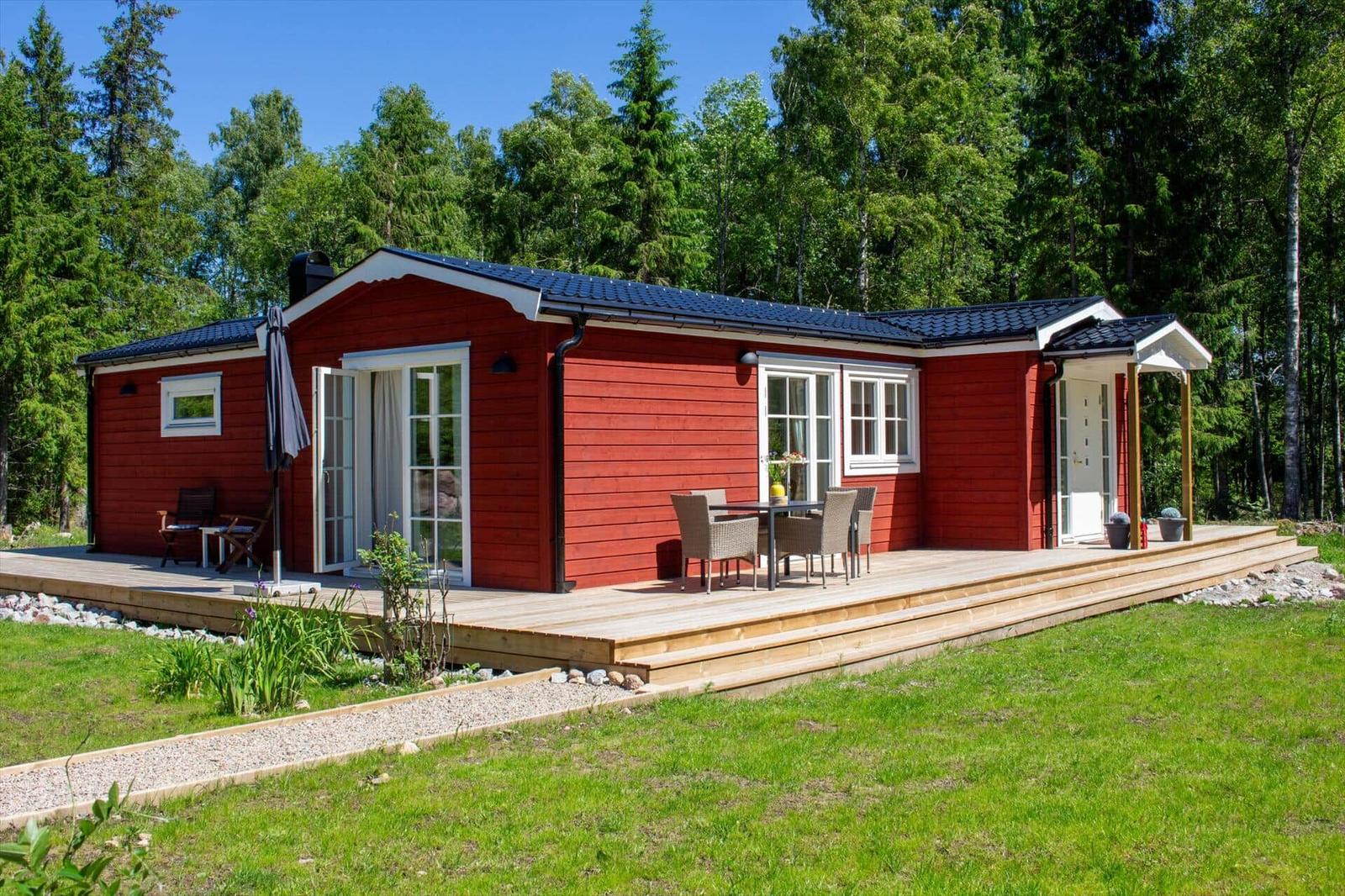 Rotes Holzhaus mit Terrasse, Garten und Wald im Hintergrund.