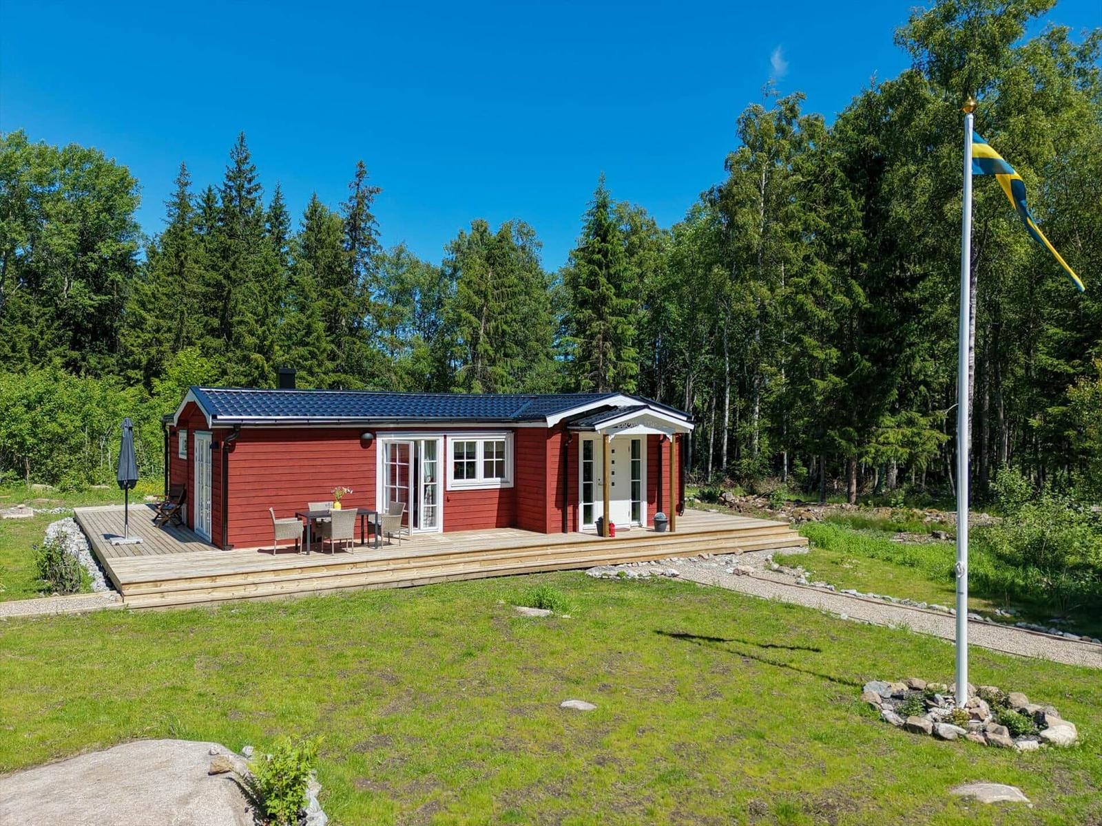Rotes Ferienhaus mit Terrasse und schwedischer Flagge im Wald