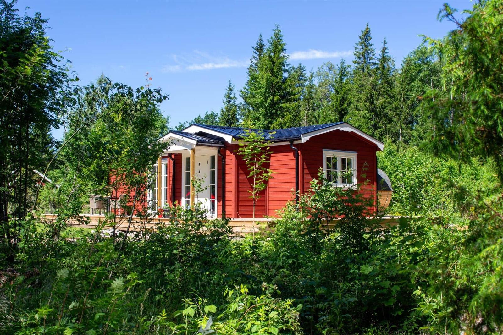 Rotes Holzhaus mit weißen Fenstern und Terrasse im Wald.