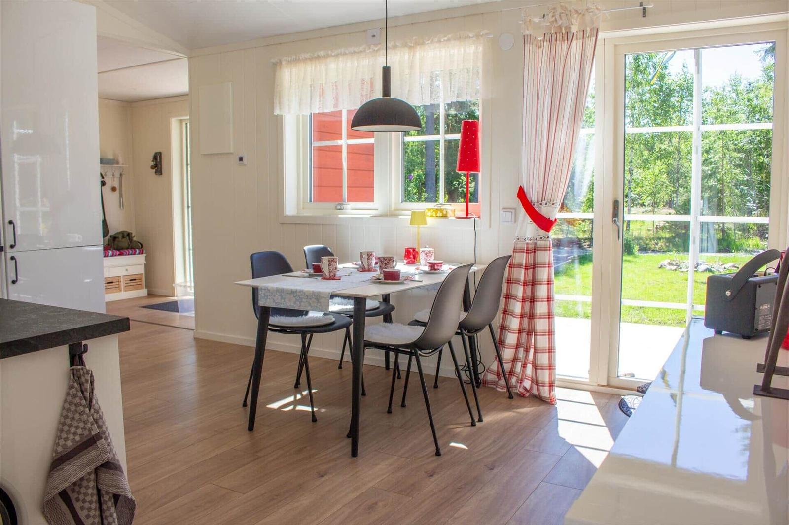 Esszimmer mit Tisch, Stühlen und Blick auf Garten. Rote Gardinen und Lampe.