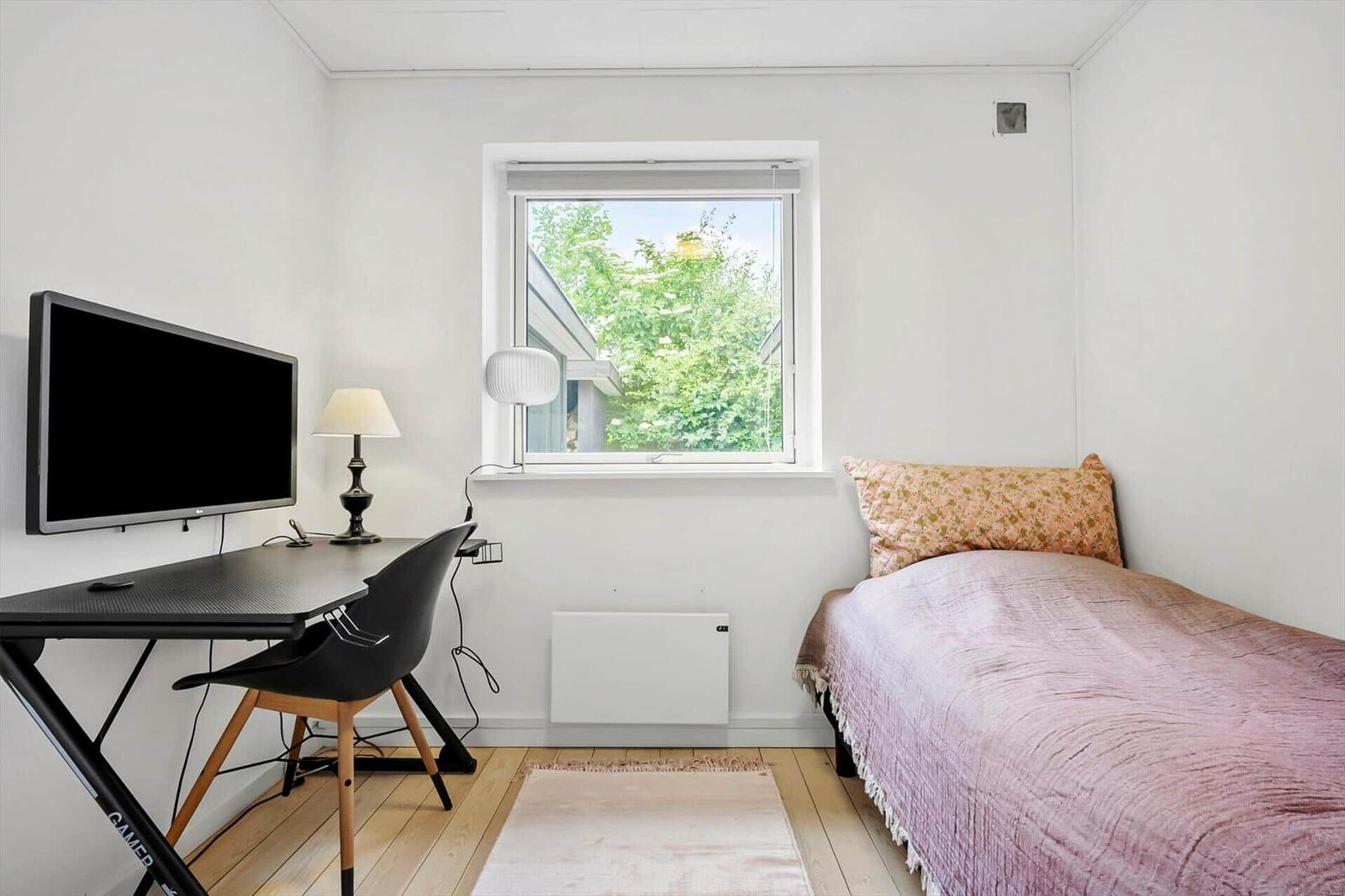 Ein Zimmer mit Bett, Schreibtisch, Fernseher und Fenster mit Blick auf Bäume.