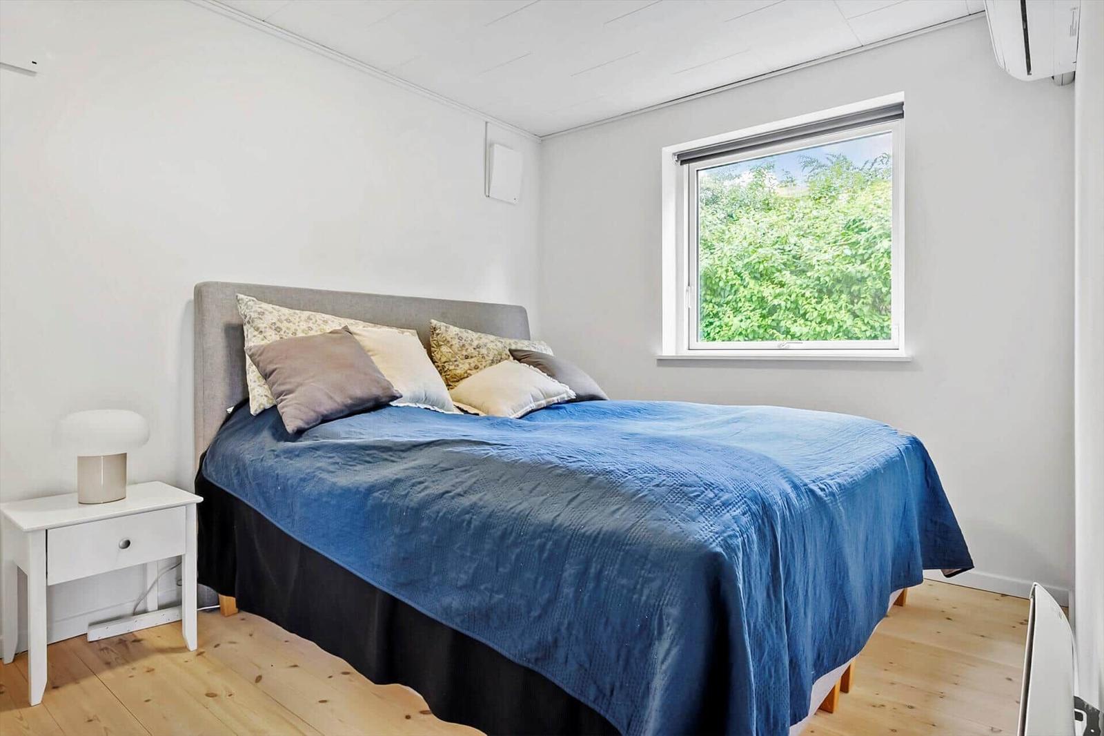 Schlafzimmer mit Bett, Nachttisch und Fenster zum Grün.