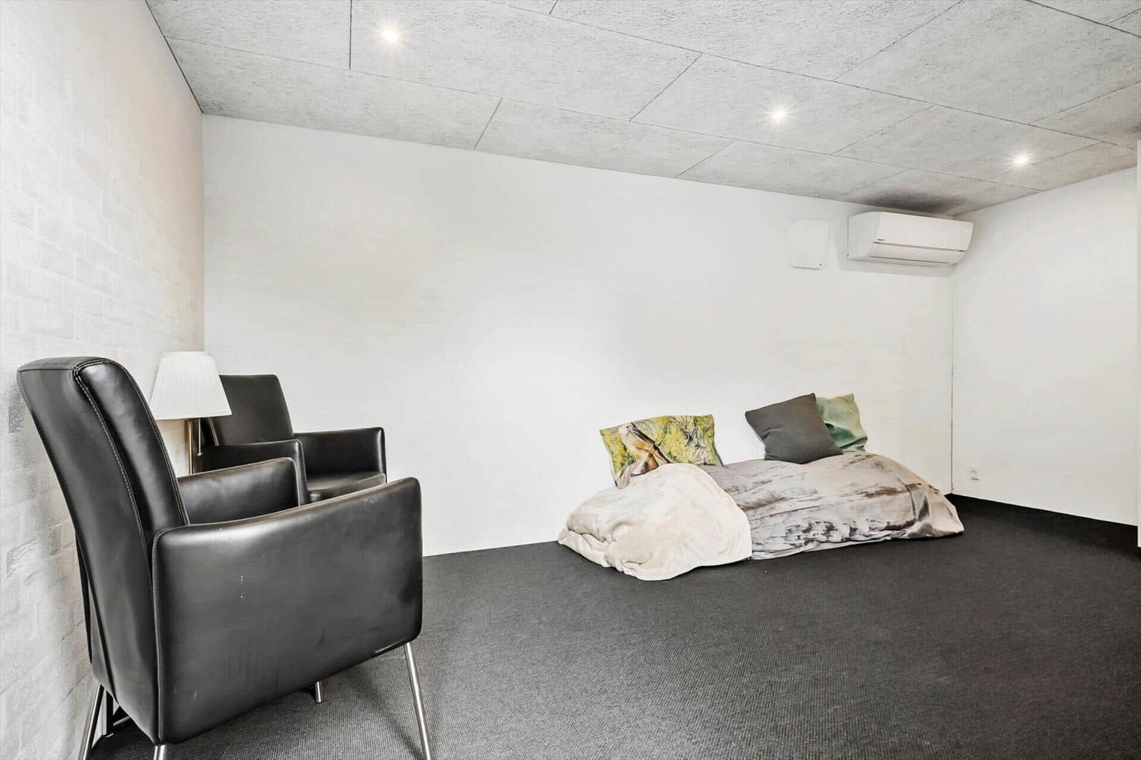Raum mit zwei schwarzen Sesseln, Bett und Klimaanlage an der Wand.
