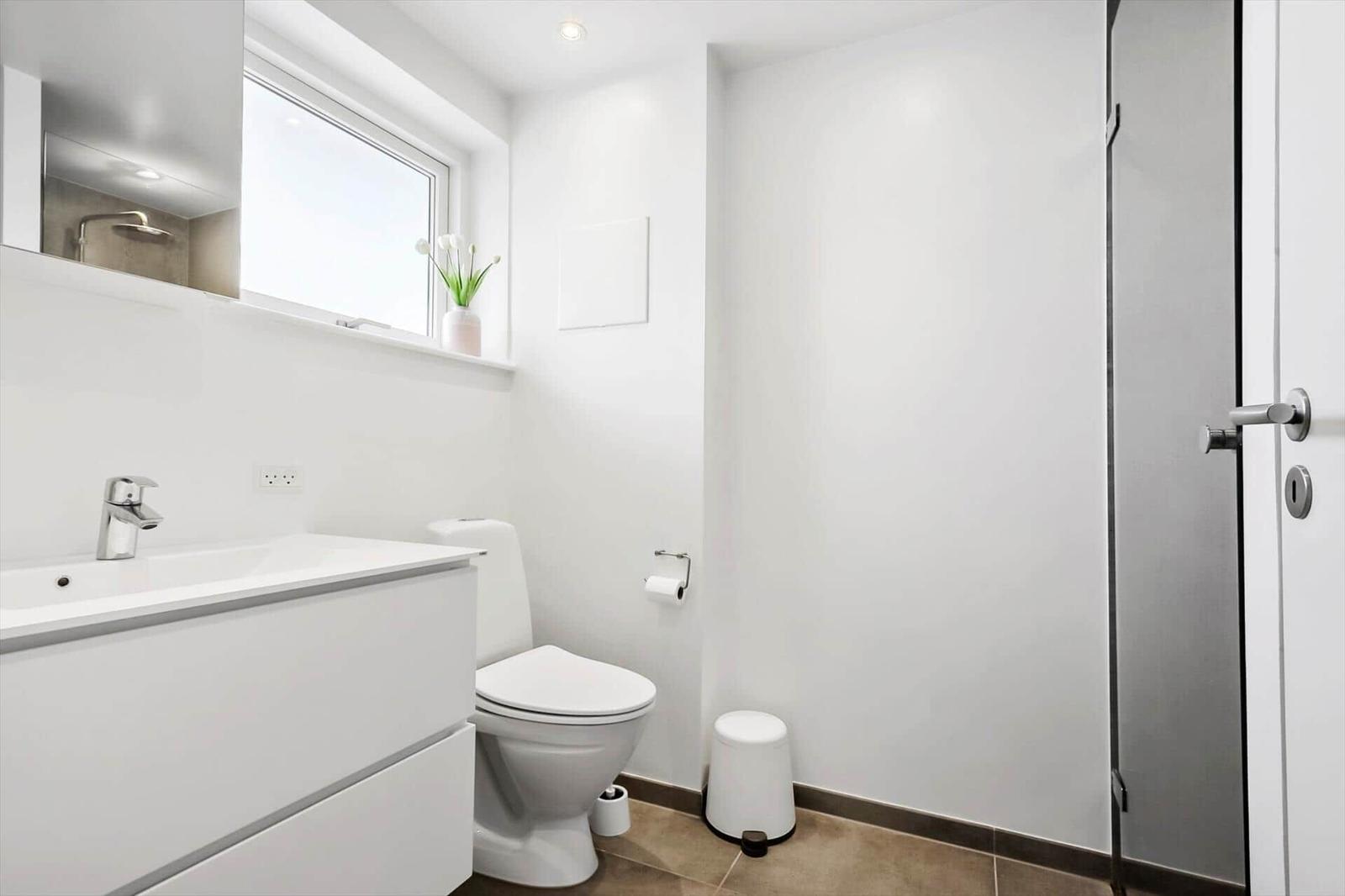 Badezimmer mit Toilette, Waschbecken und Dusche. Fenster mit Blumen auf dem Sims.