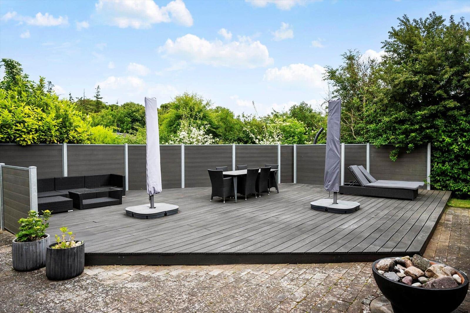 Terrasse mit Sitzgruppe, Esstisch und Liegen. Umgeben von Grün und Zaun.