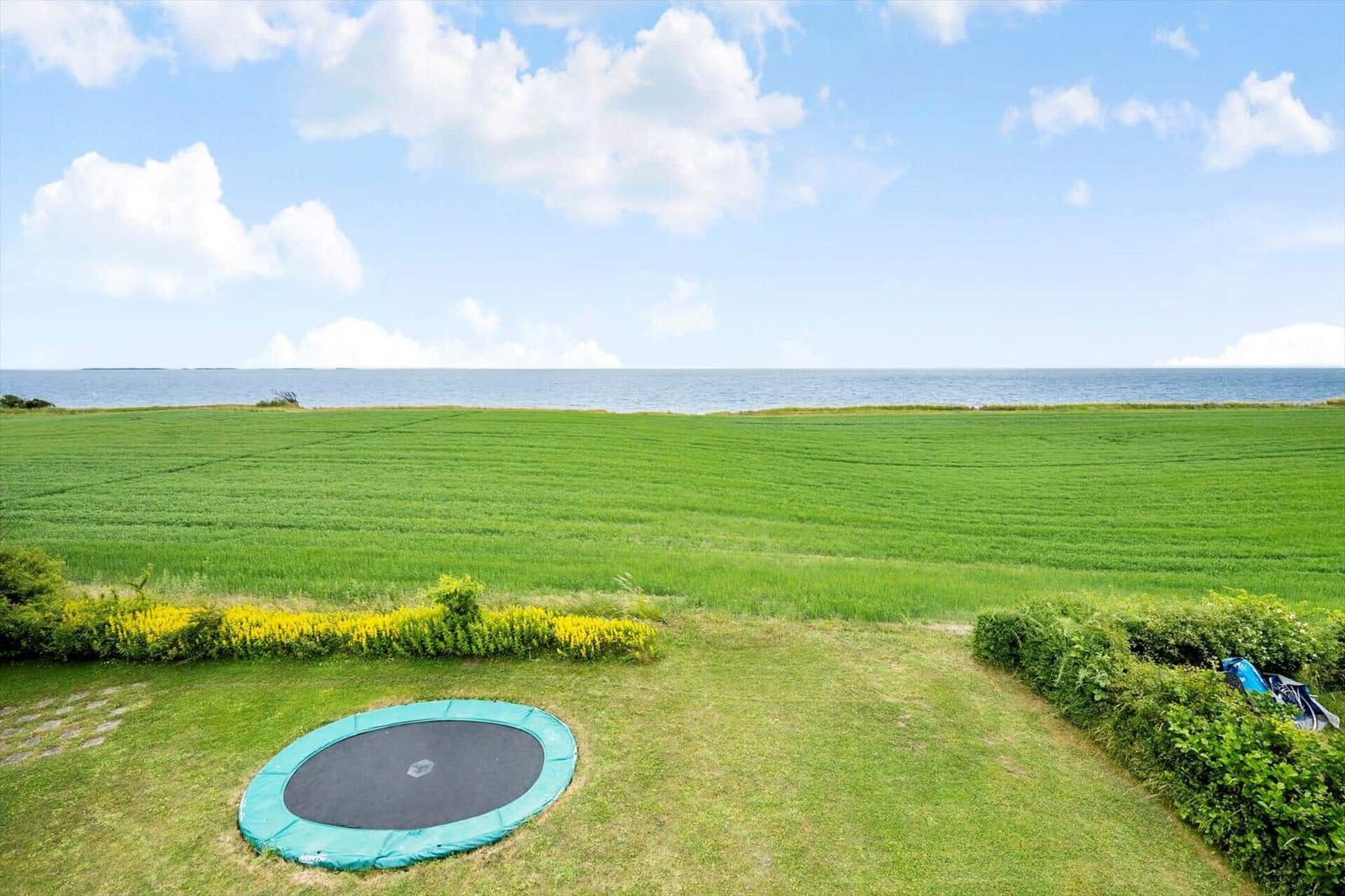 Grünes Feld mit Trampolin und Blick auf das Meer.