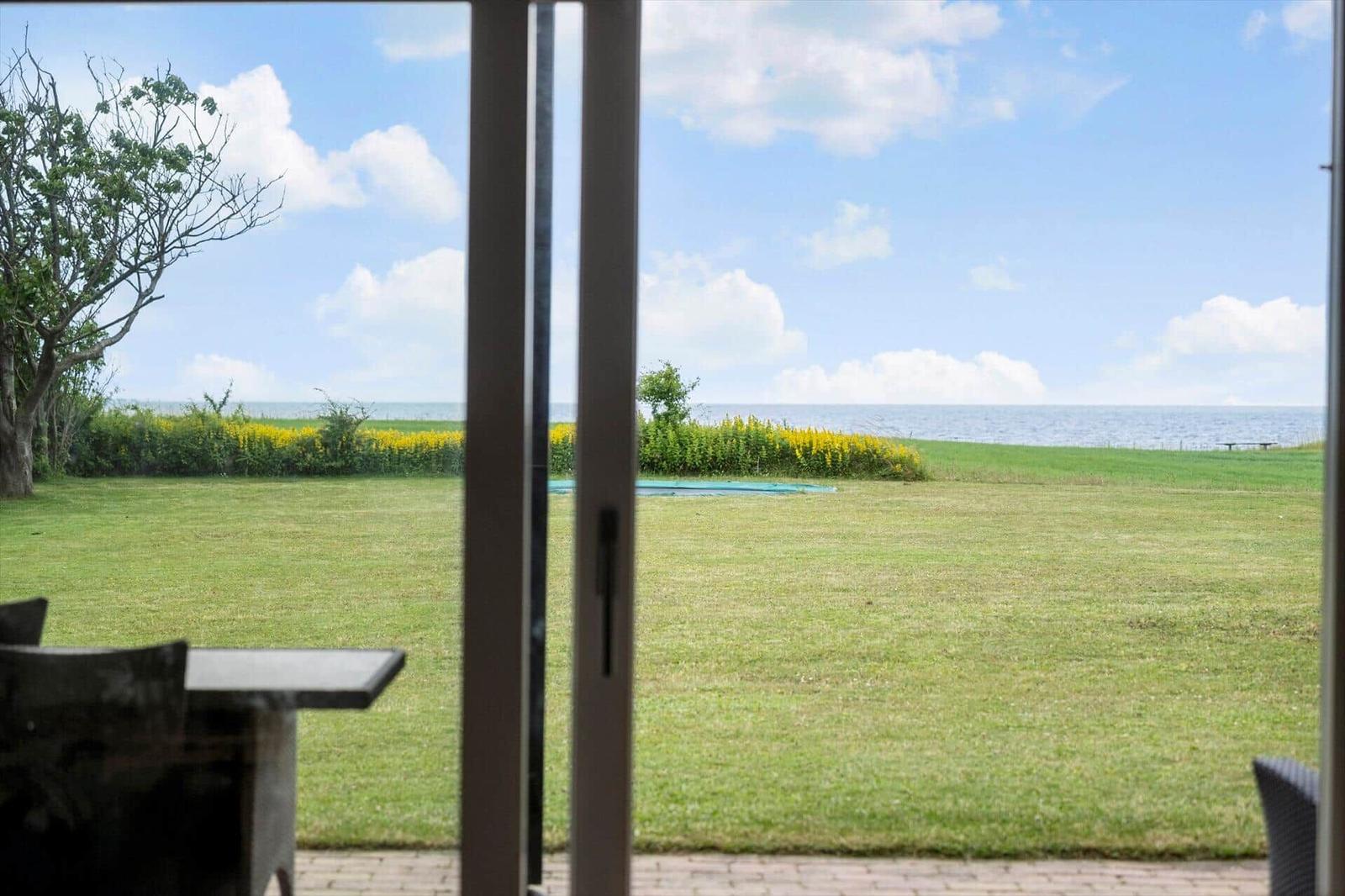 Von der Terrasse aus Blick auf grünen Rasen, gelbe Blumen und das Meer unter blauem Himmel.