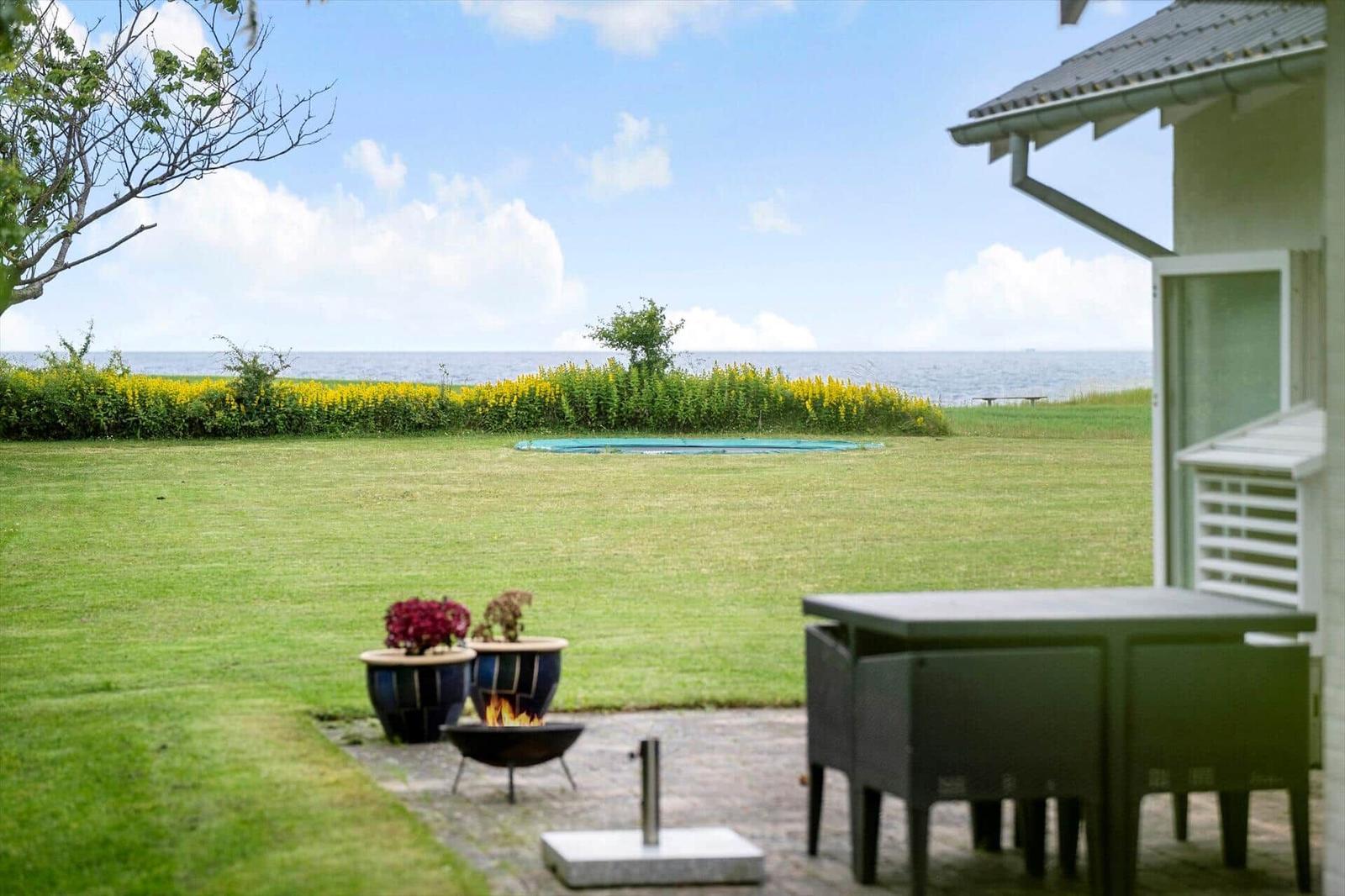 Außenbereich mit Grill, Tisch und Blick auf Meer und Grasfläche.