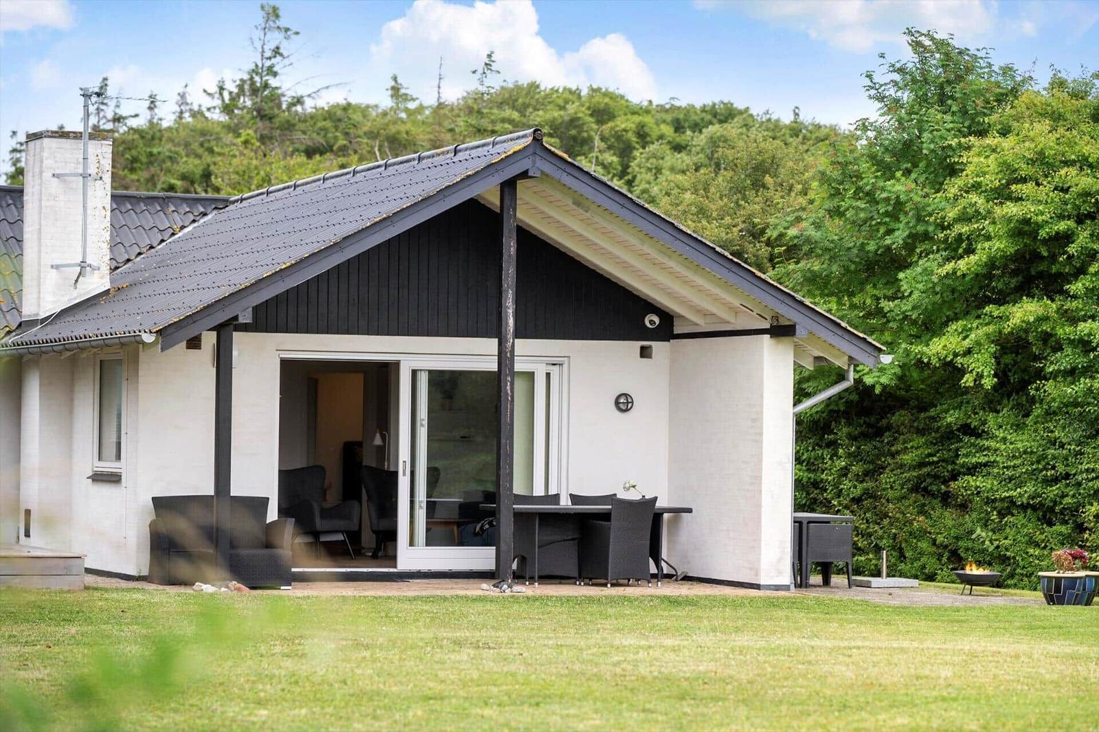 Moderne Villa mit Terrasse, Sitzgelegenheiten und Garten. Hintergrund: grüne Bäume.