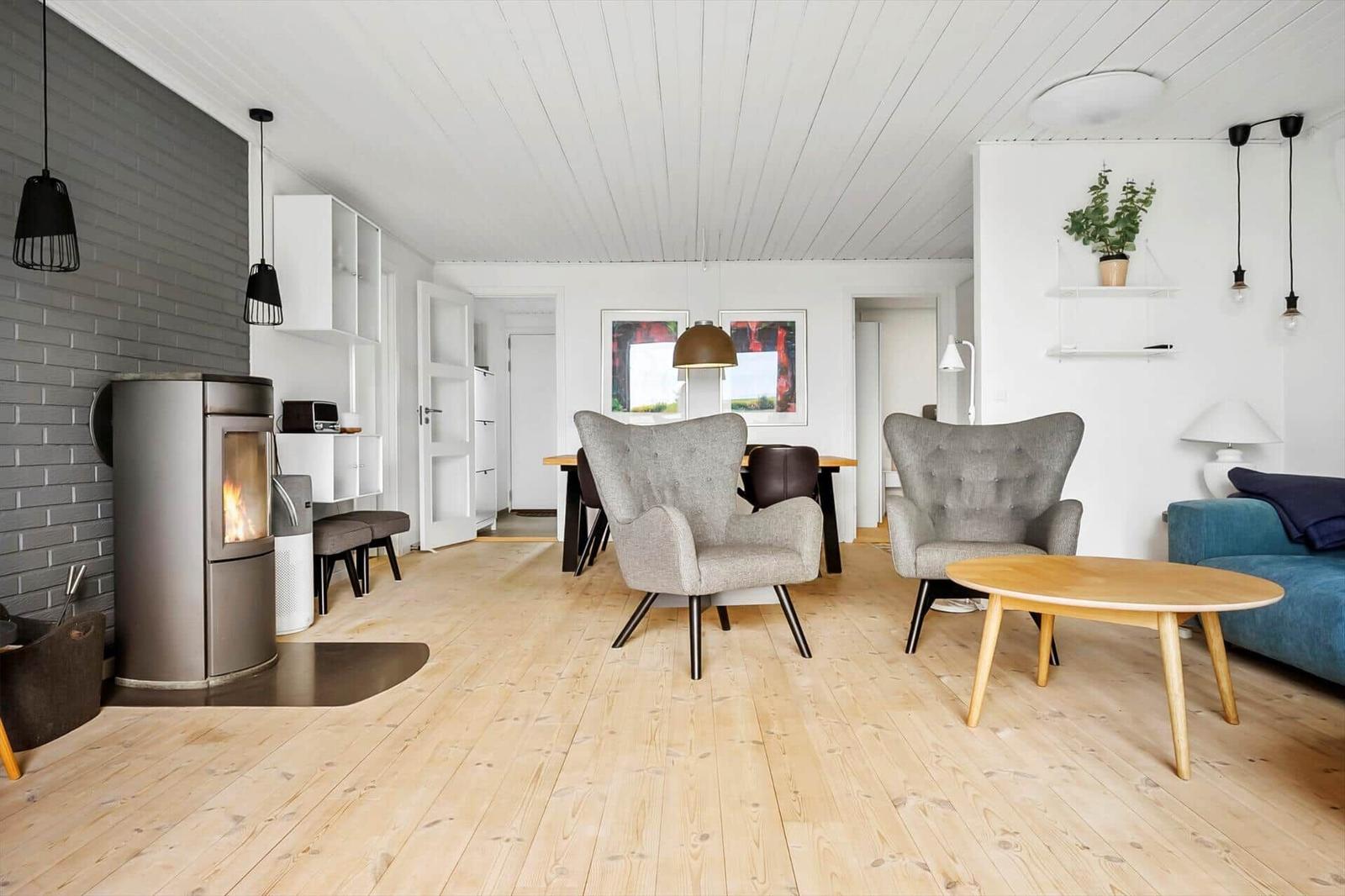 Wohnzimmer mit Holzboden, Kamin und Sesseln. Essbereich und Küche im Hintergrund.