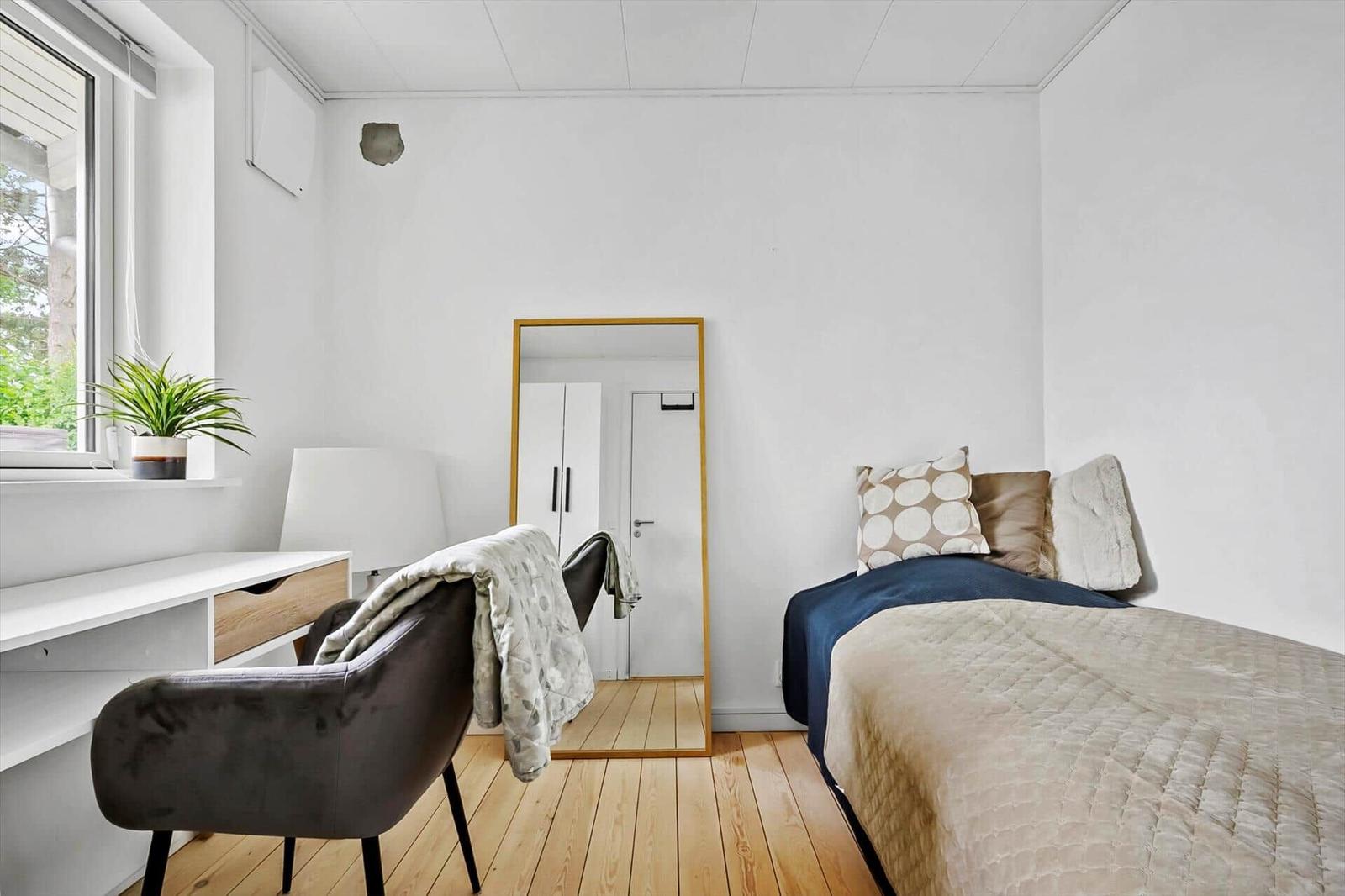 Schlafzimmer mit Bett, Spiegel, Schreibtisch und Pflanze an Fenster