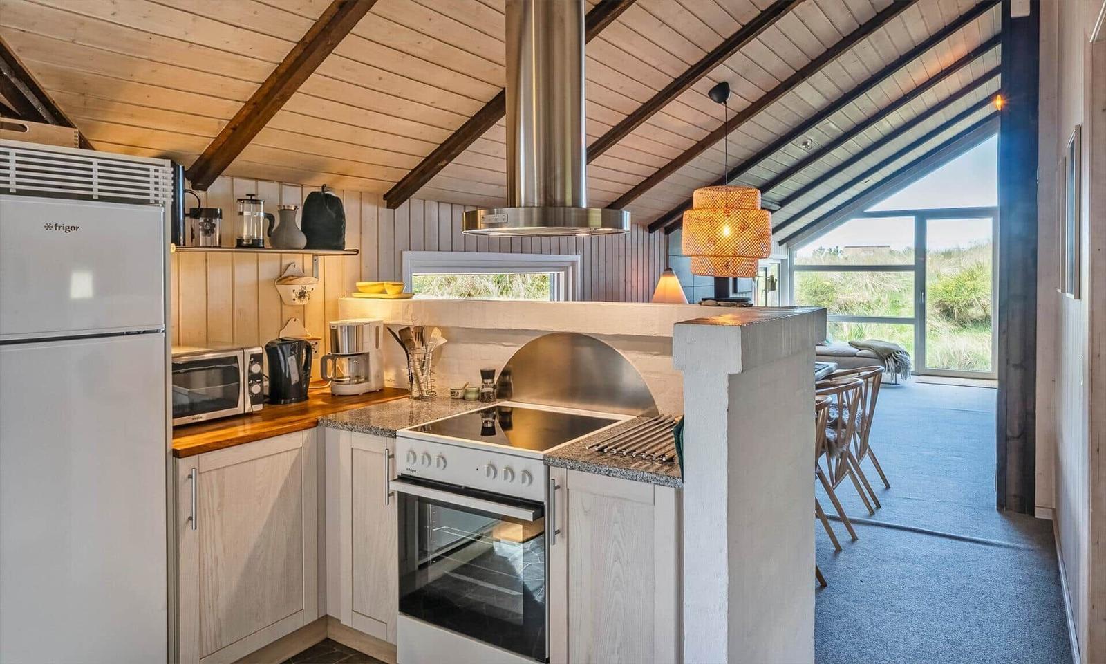 Küche mit Holzboden, Edelstahlherd und Blick auf Wohnbereich.