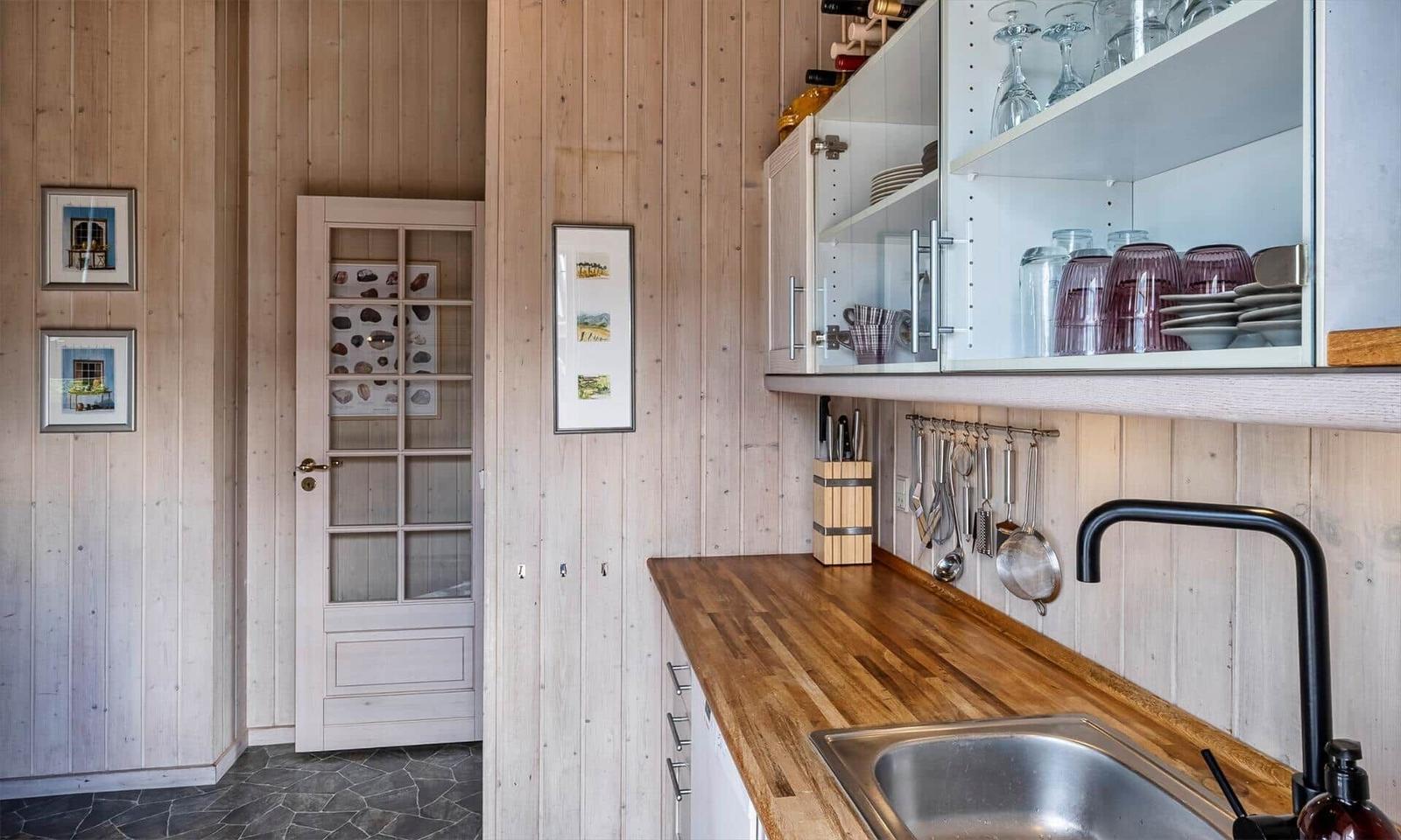 Küche mit Holzwand, Edelstahlspüle und Glasregalen mit Geschirr.