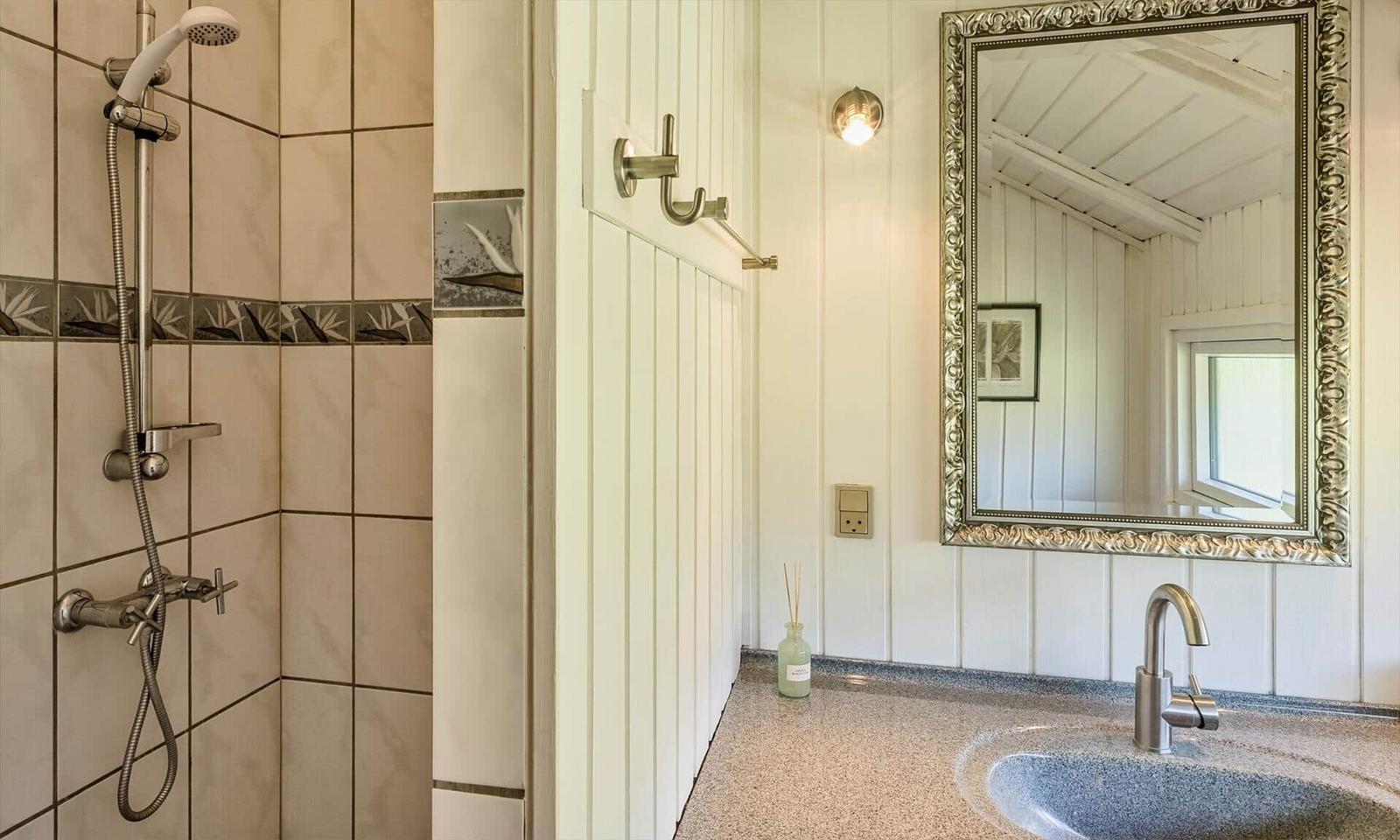 Bad mit Dusche, Waschbecken und Spiegel an weißer Wand.