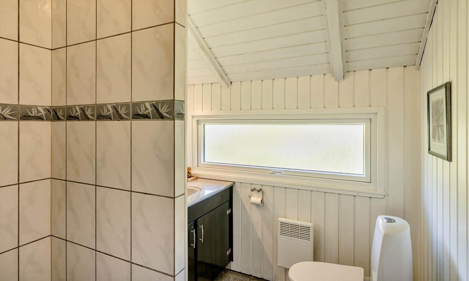 Badezimmer mit Fliesenwand, Waschbecken und Toilette unter einem schrägen Dach